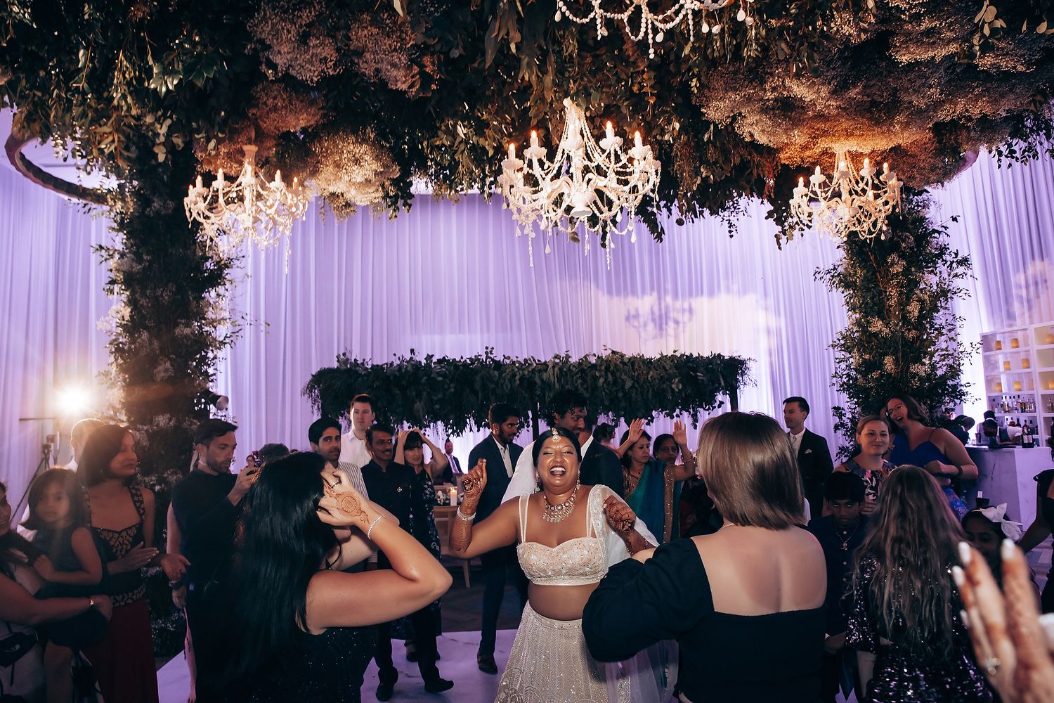 Wedding reception dance floor with hanging greenery and purple lighting effects.