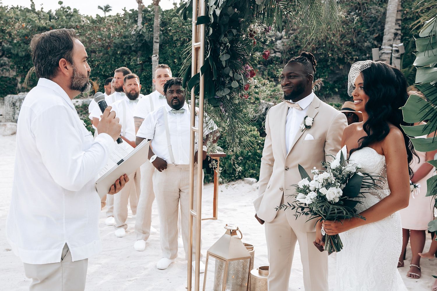 Wedding party in white and beige attire standing together at an outdoor venue.
