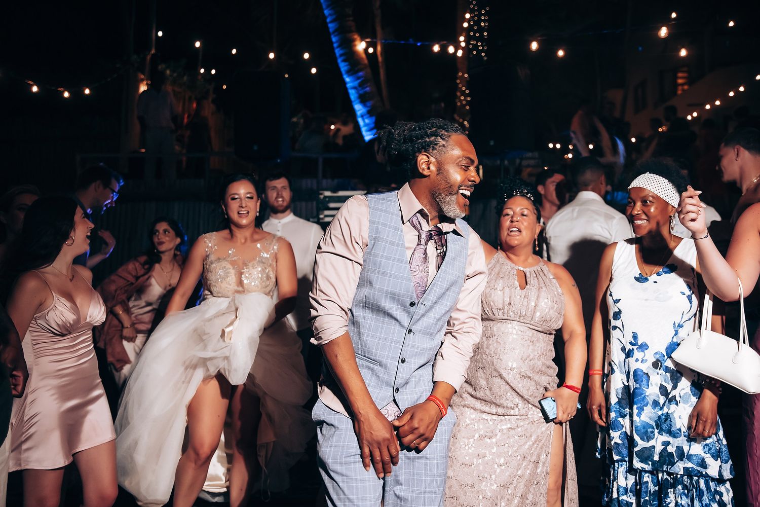 Lively dance floor at wedding reception with guests in formal attire under string lights.