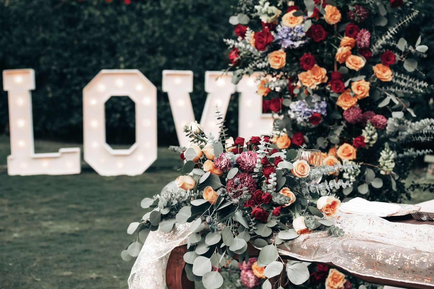 Colorful floral arrangement with roses next to illuminated LOVE letters at a wedding.