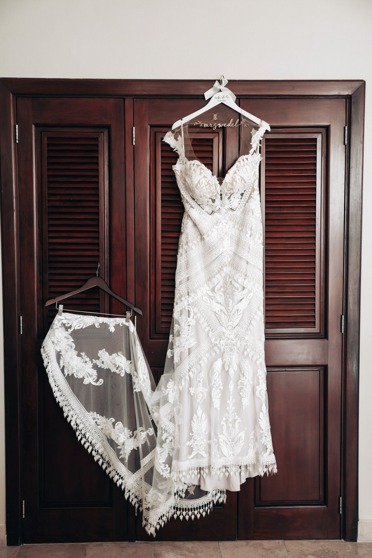 Elegant lace wedding dress and veil hanging on a dark wood wardrobe closet at Dreams Tulum