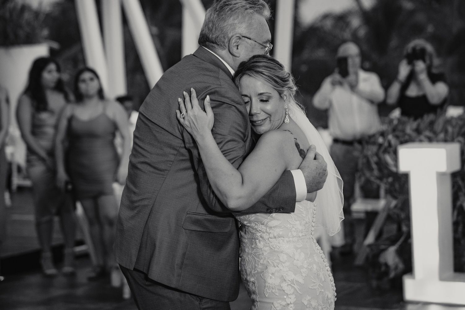 Emotional black and white photo of bride sharing tender father-daughter dance at outdoor reception.