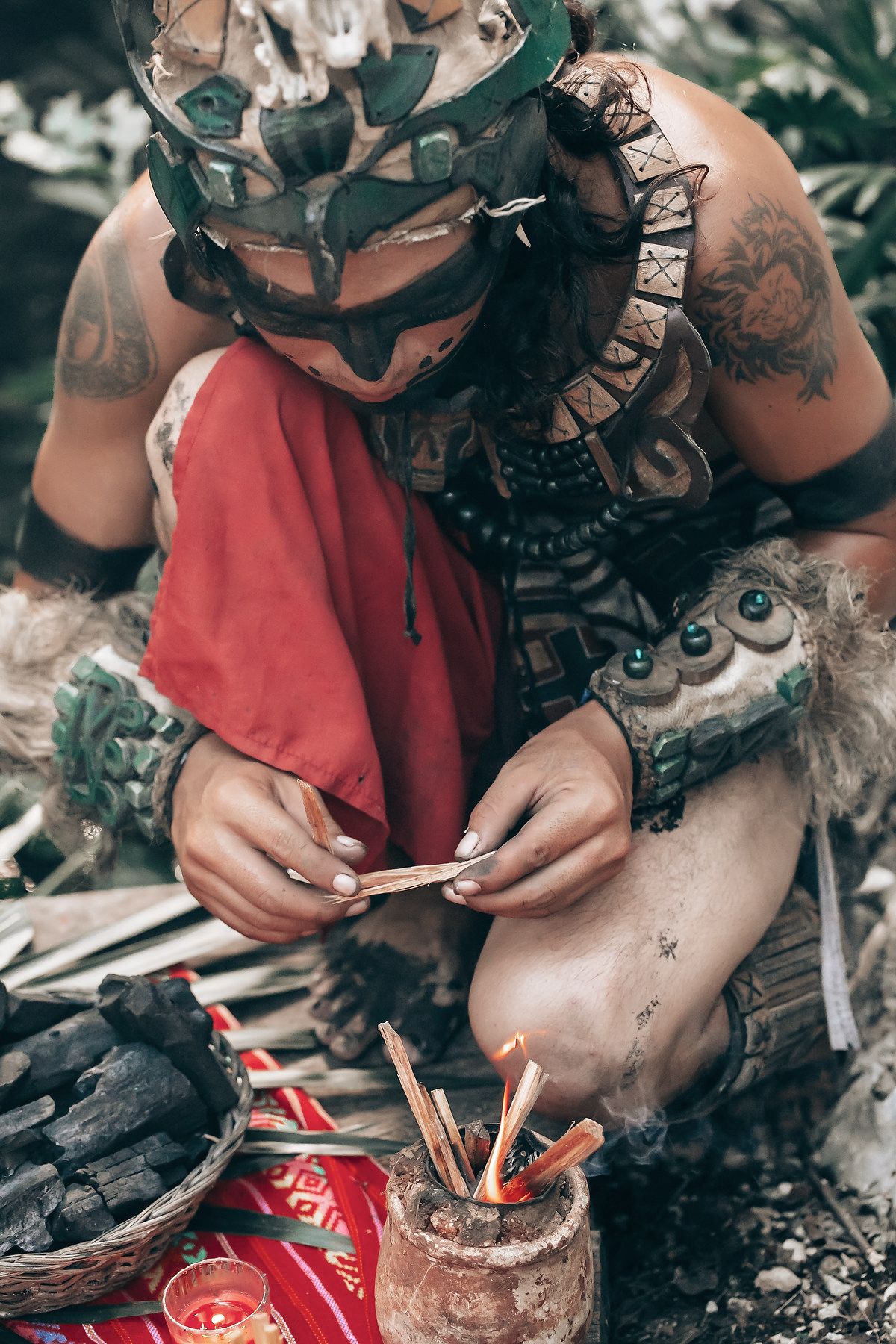 A person wearing elaborate tribal-inspired attire sits on the ground, holding various items.
