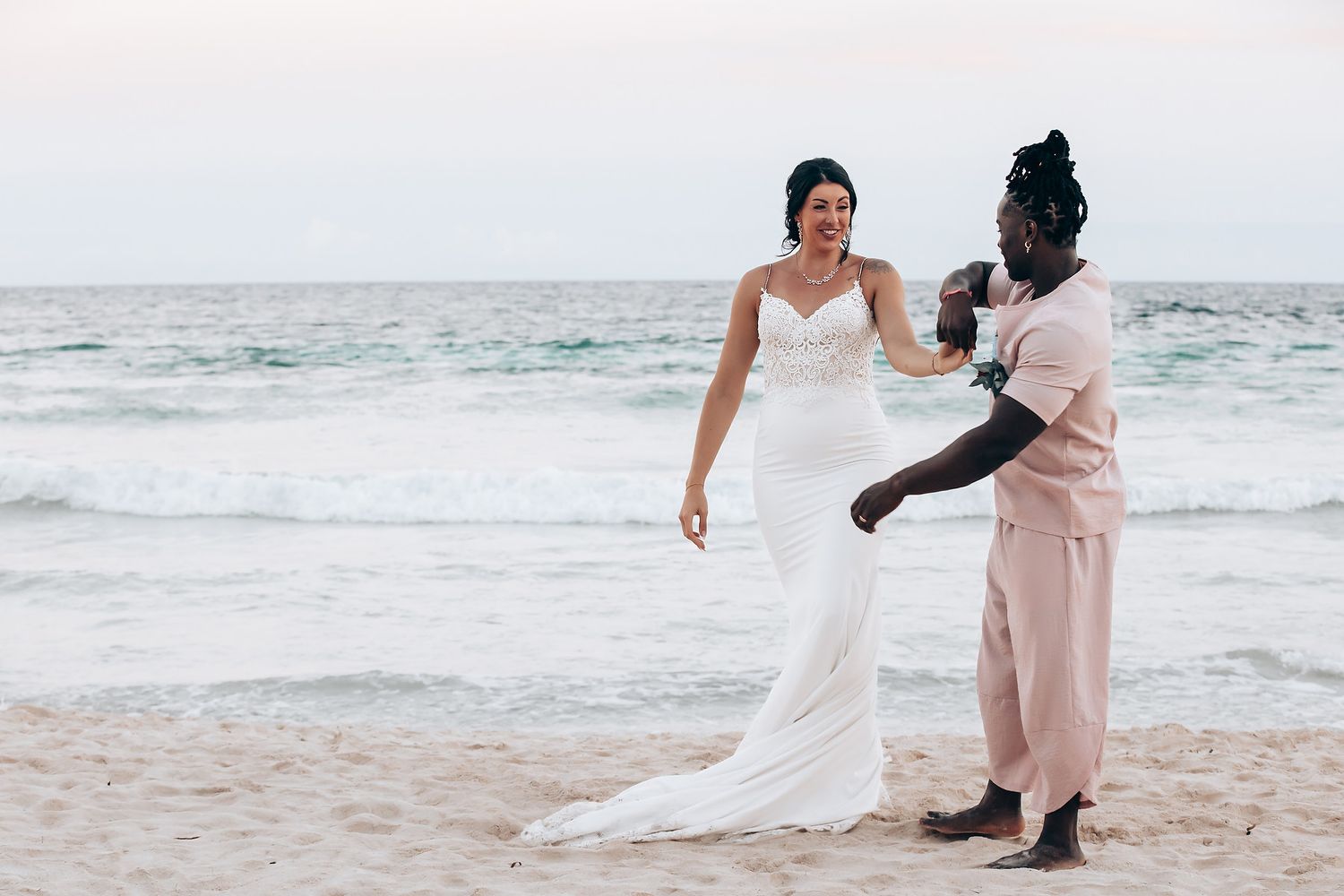 A bride and her companion walking on the beach in their wedding attire.