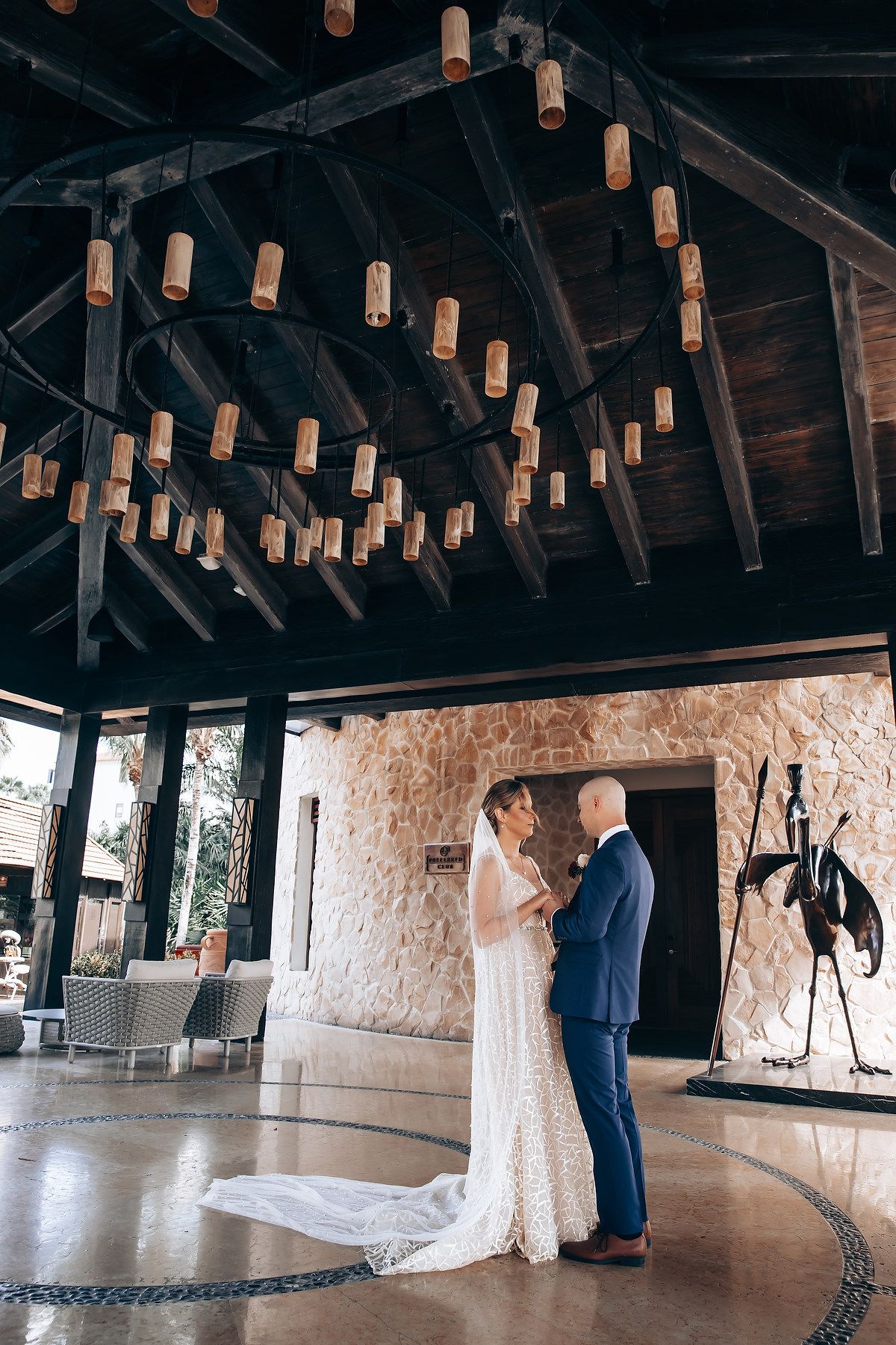 A bride and groom embrace on their wedding day in a dimly lit room with hanging lights.