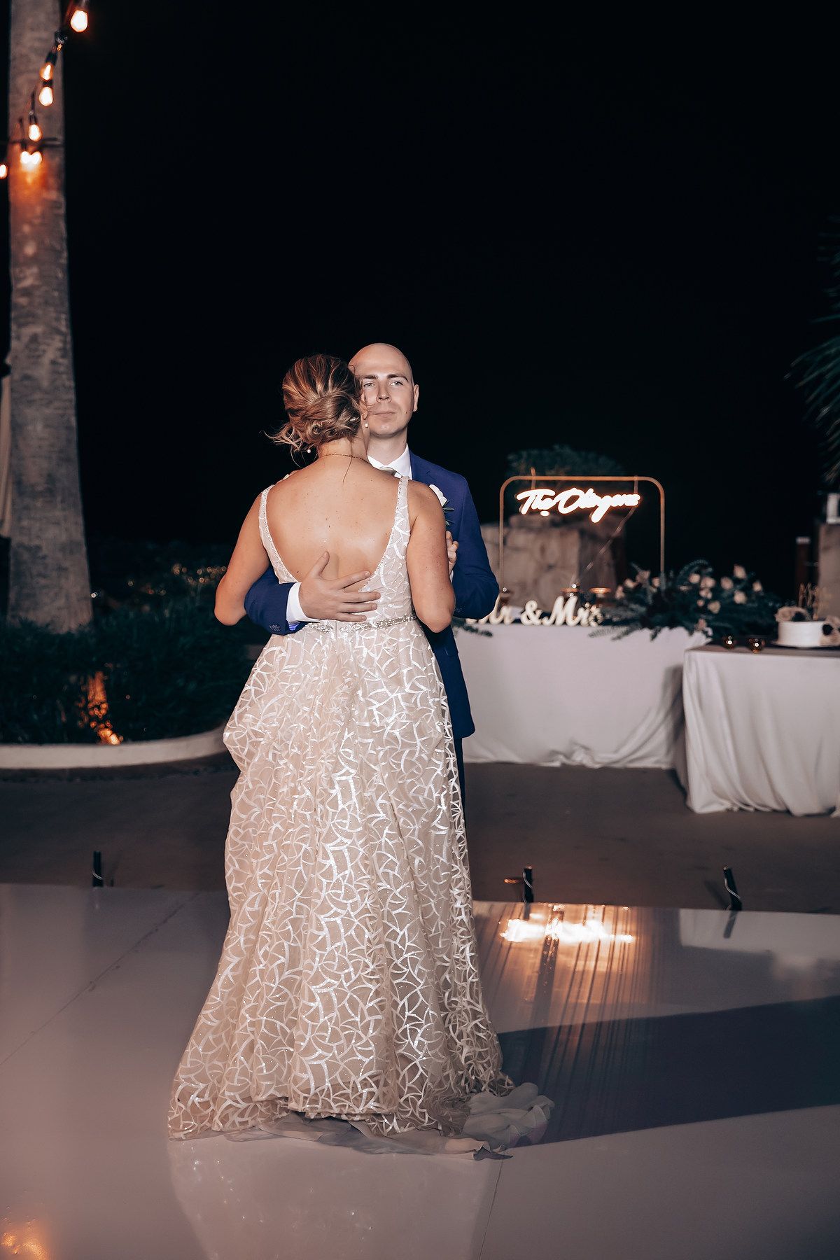 A woman in a long, shimmering white dress dancing at a wedding reception at night.