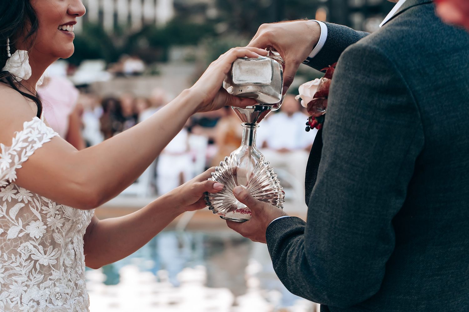 Two people in wedding attire clink champagne glasses during an outdoor celebration.