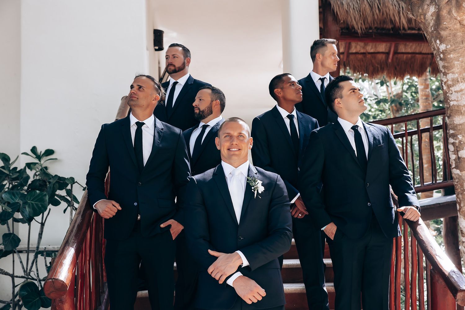 Groomsmen in black suits posing together at a destination wedding venue.