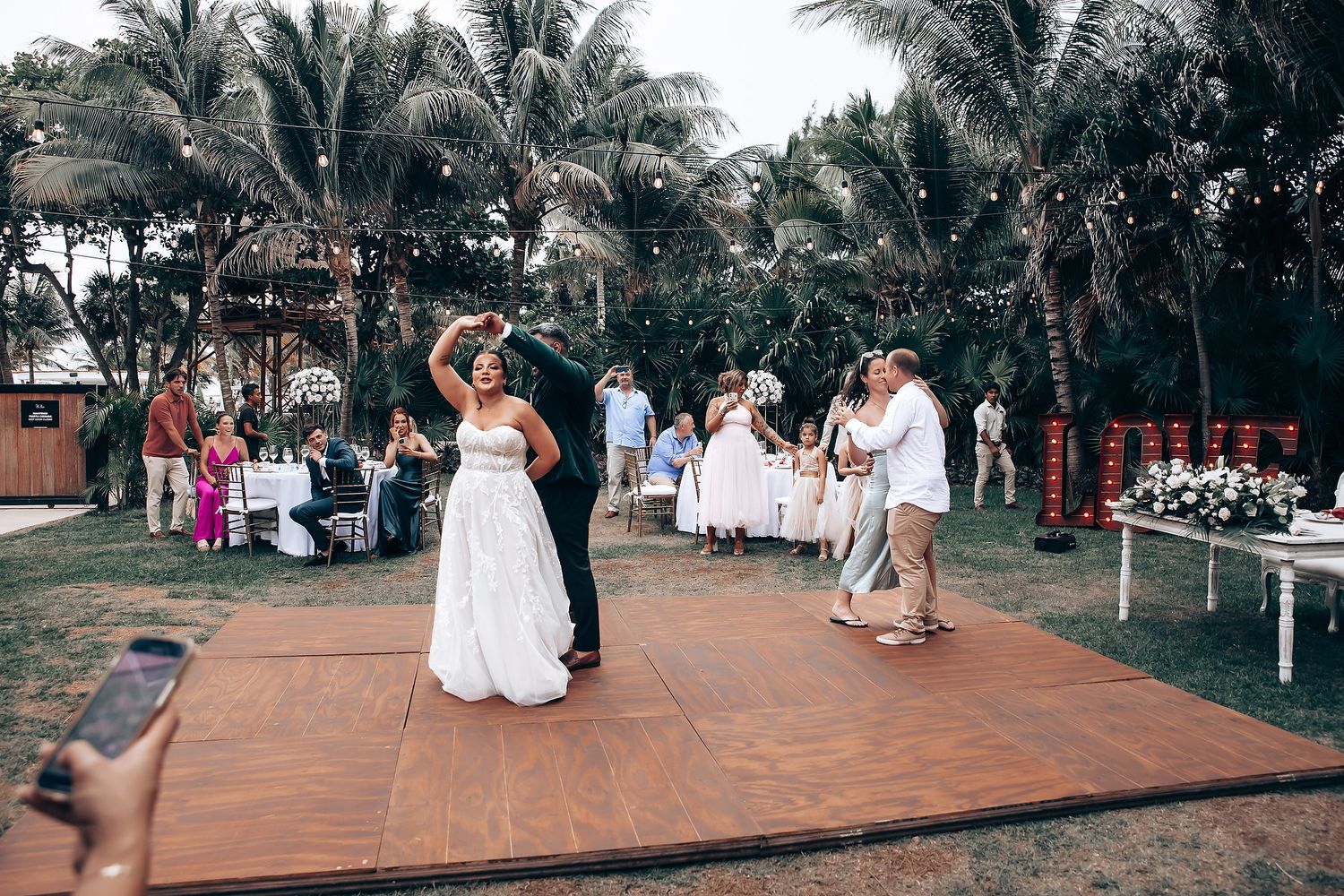 Outdoor wedding reception with palm trees and wooden dance floor setup.