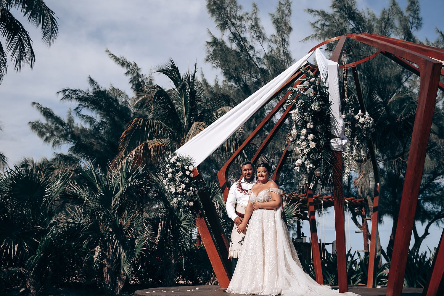 A couple dances together at a tropical beach wedding venue with palm trees and white decor.