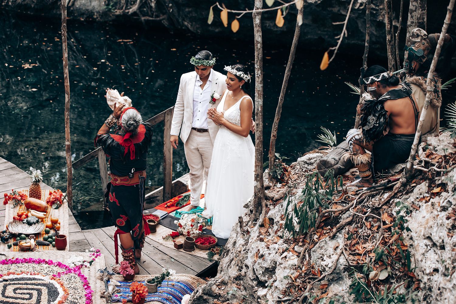 A ceremonial gathering on a wooden platform in a natural setting with decorative elements and offerings.