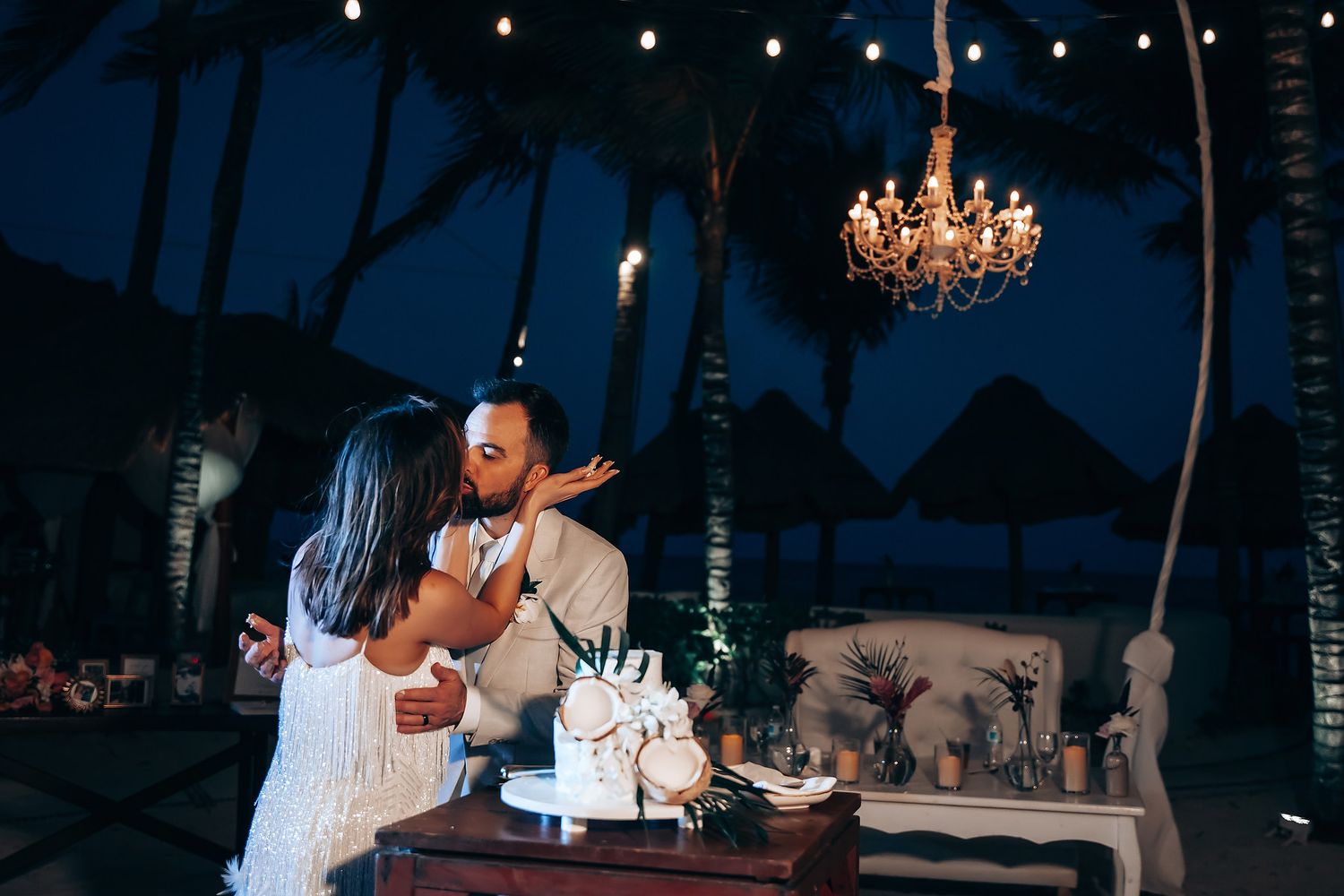 Romantic evening reception with chandelier lighting and couples dancing at a dimly lit venue.