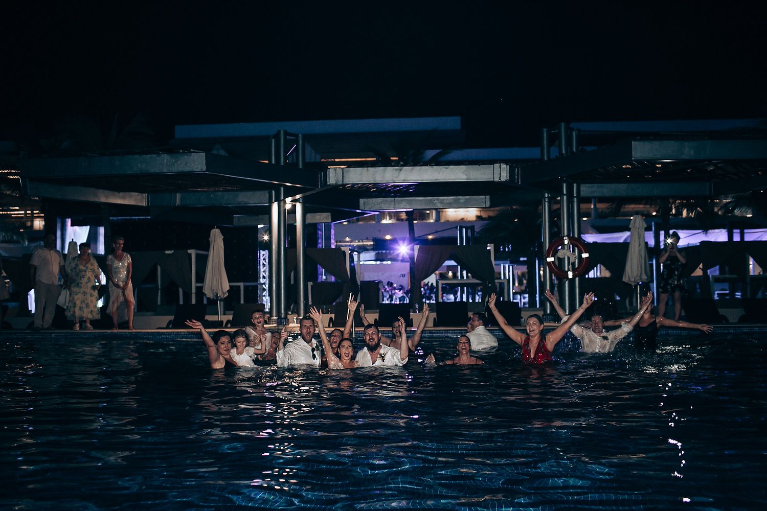 Silhouettes of people enjoying a nighttime pool party with blue lighting and reflections.