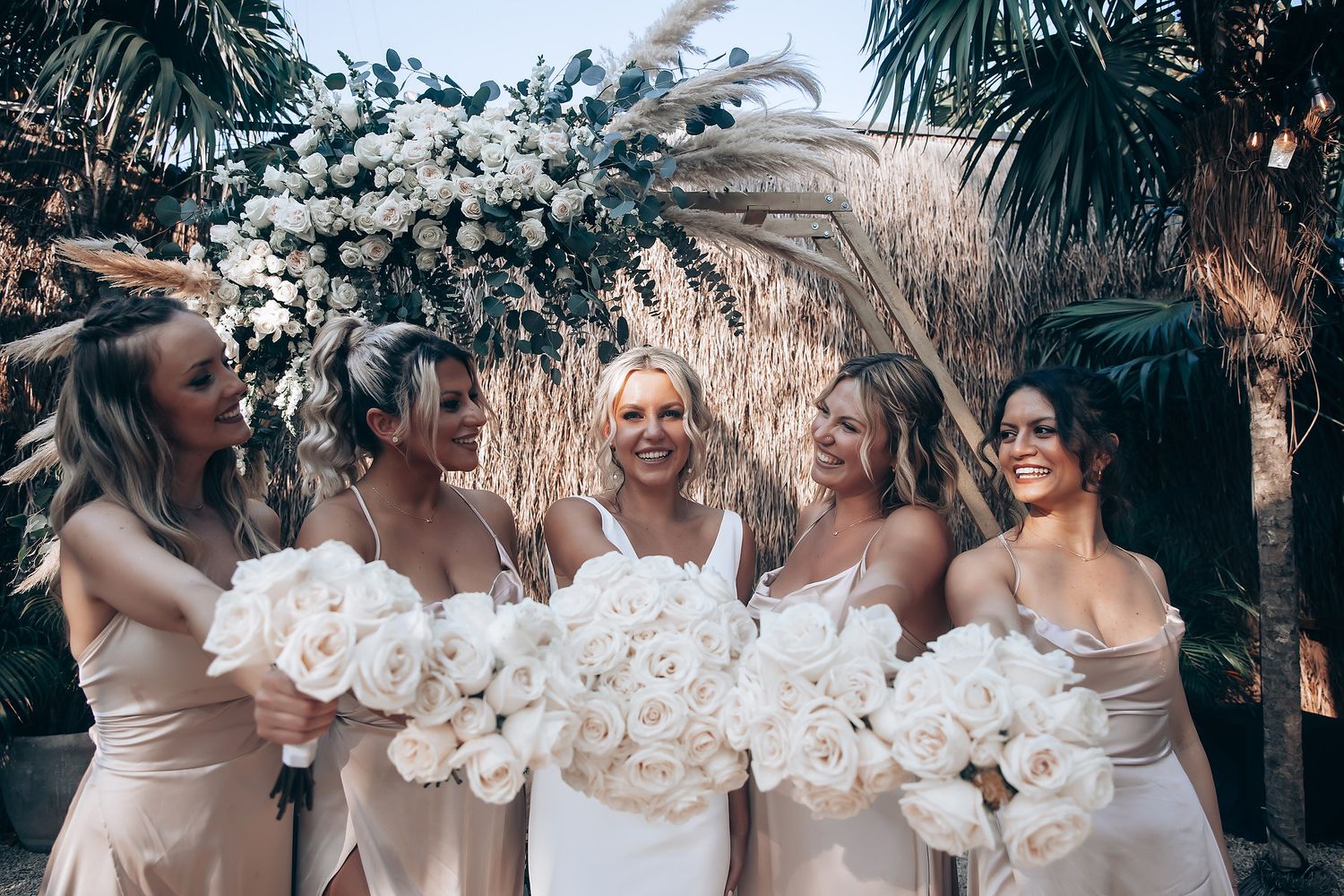 Wedding party celebrating with white floral decorations in an outdoor tropical setting.