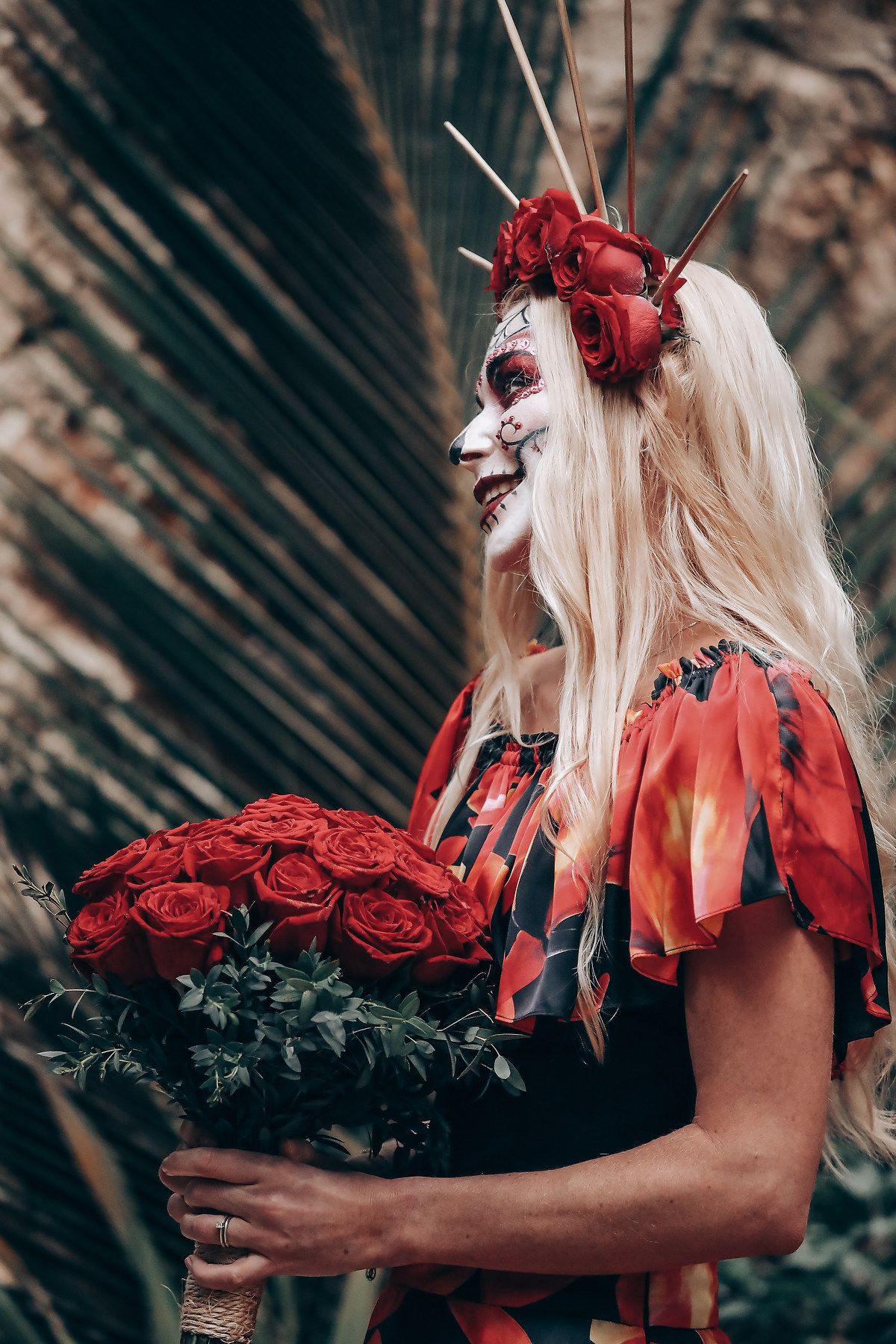 Artistic Day of the Dead themed photoshoot featuring red roses and gothic Halloween makeup in a dark forest setting.