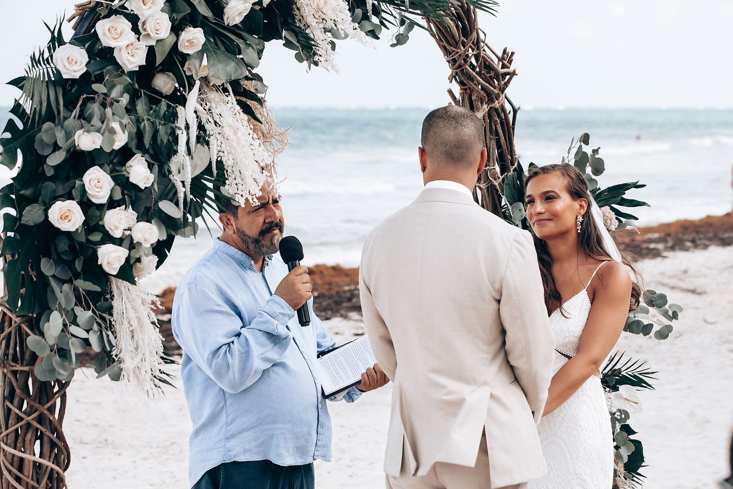 Wedding ceremony photos on a beach with white floral arrangements and tropical greenery.