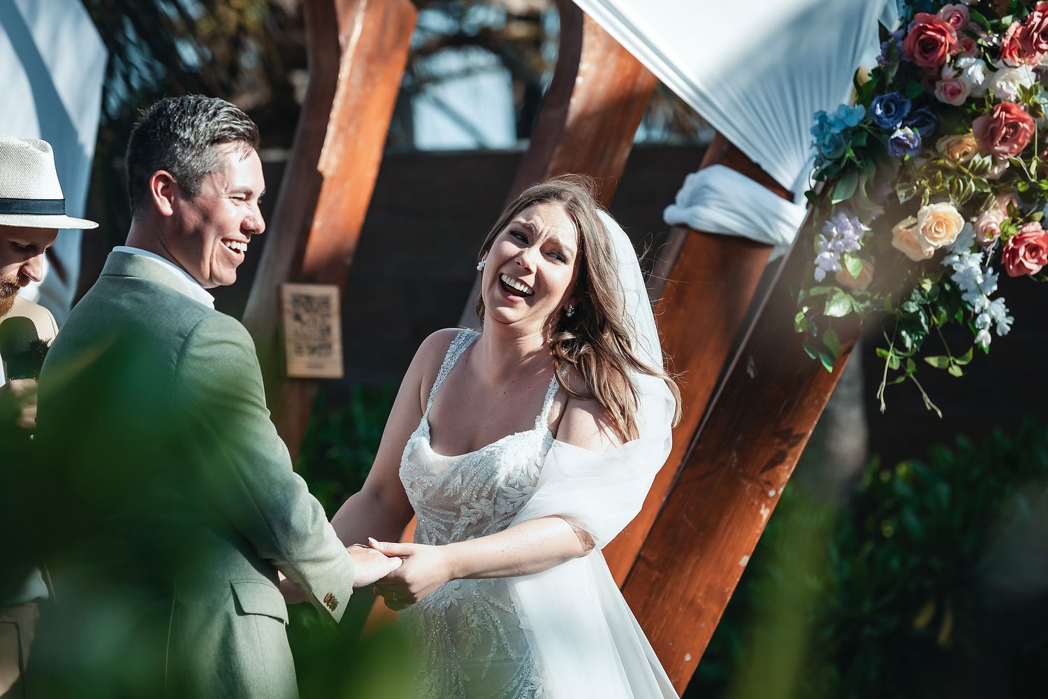 Bride and groom laughing joyfully while holding hands at outdoor wedding ceremony altar.
