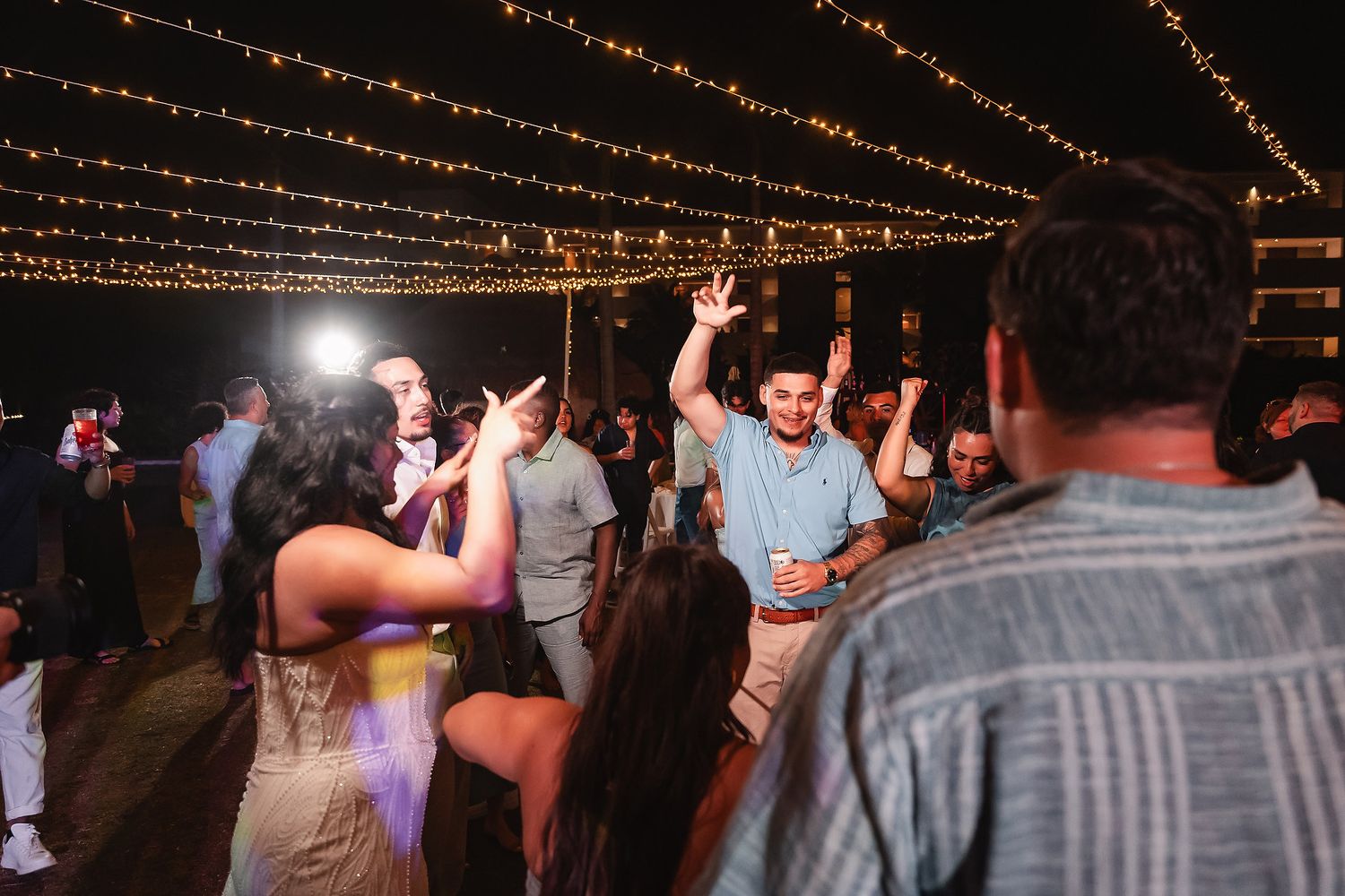 Guests dancing under string lights at an outdoor wedding reception at night.