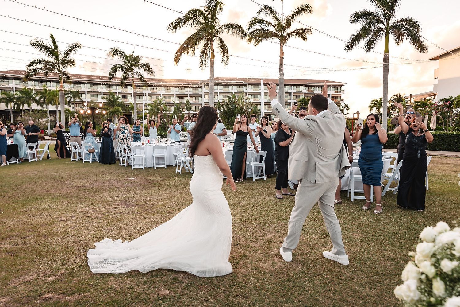 Bride and groom celebrate grand entrance with raised hands at elegant outdoor tropical wedding reception.