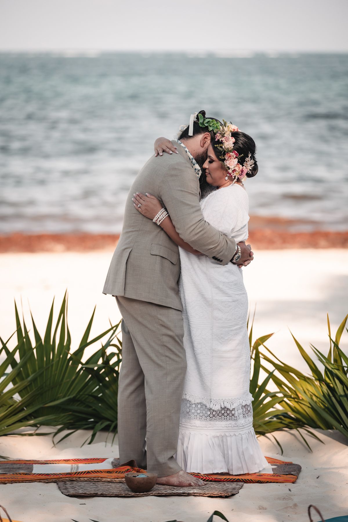 Couple sharing a romantic first kiss on a sandy beach during their outdoor wedding ceremony with ocean backdrop.