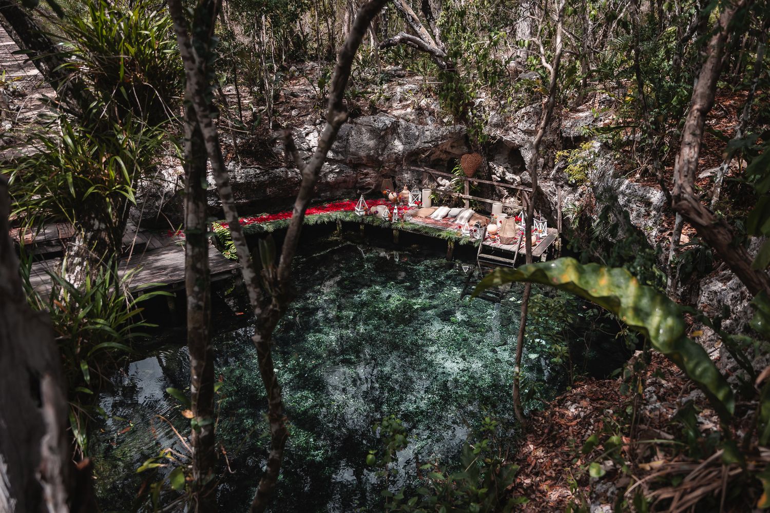 Aerial view of a crystal-clear cenote surrounded by lush jungle trees and a wooden platform in Mexico.