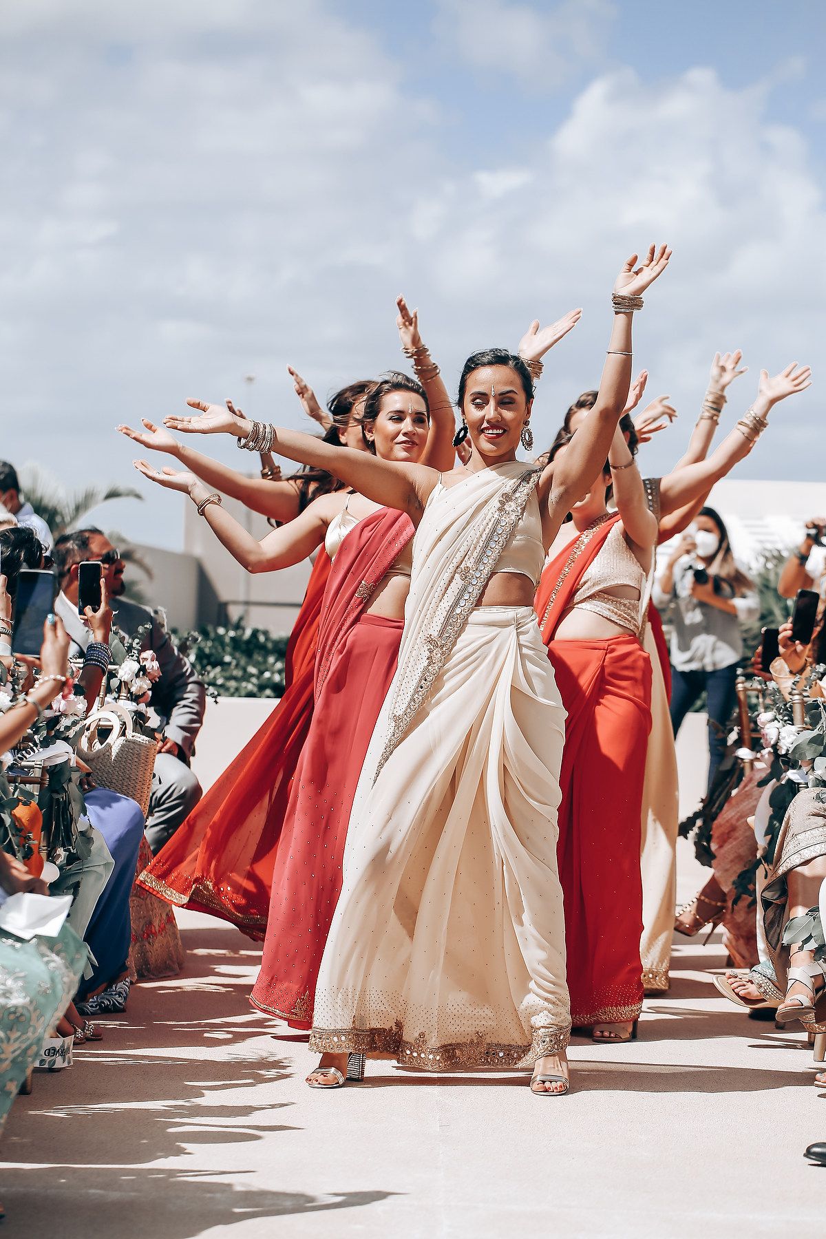 Wedding party in coral and cream dresses dancing with arms raised in celebration.