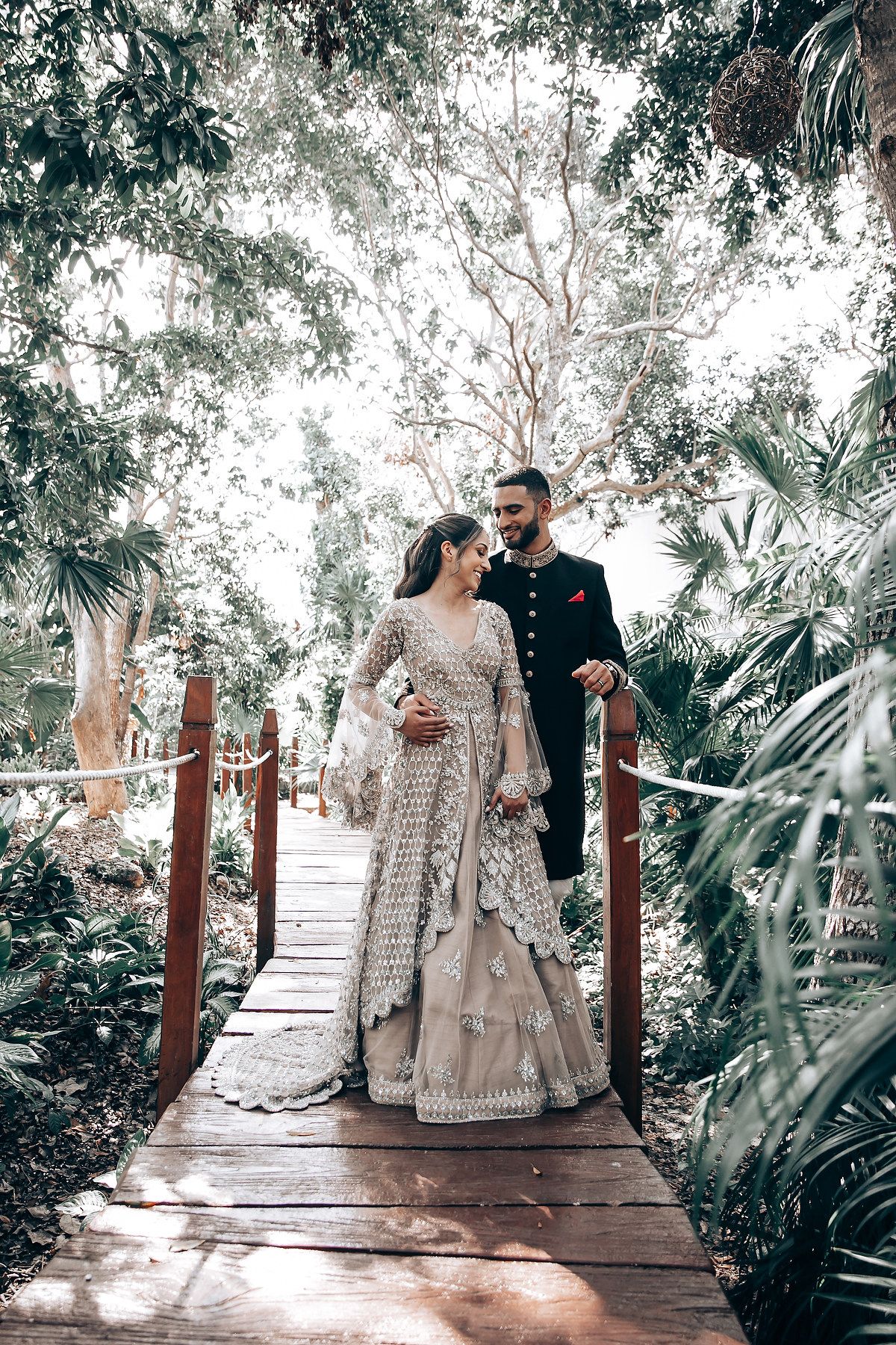 Couple sharing intimate moment on wooden walkway surrounded by lush tropical greenery.