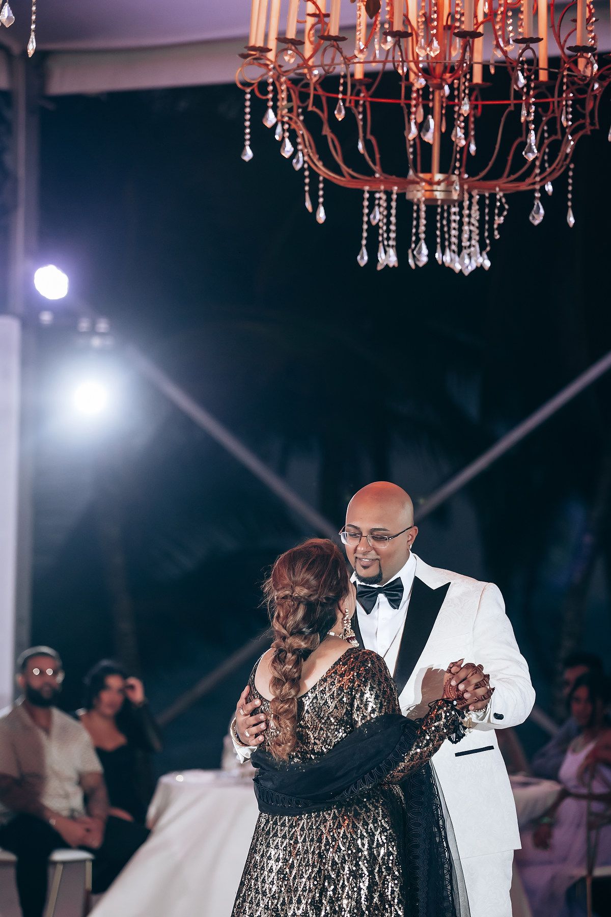 Formal dance between two people under elegant crystal chandeliers at an evening event.