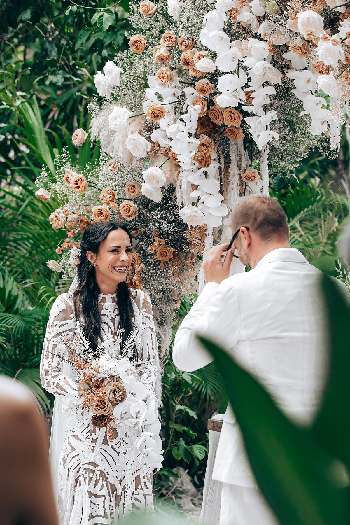 Intimate wedding ceremony moment under an arch decorated with peach and white flowers.