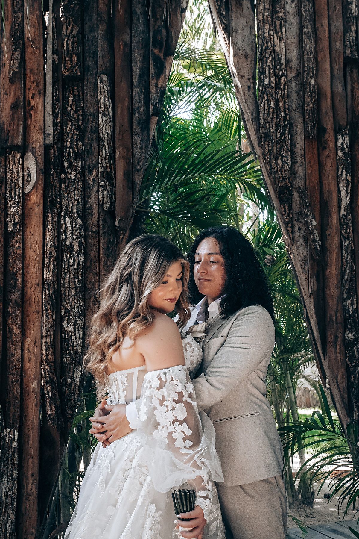 Intimate wedding portraits with a couple embracing against a backdrop of wooden walls and palm leaves.