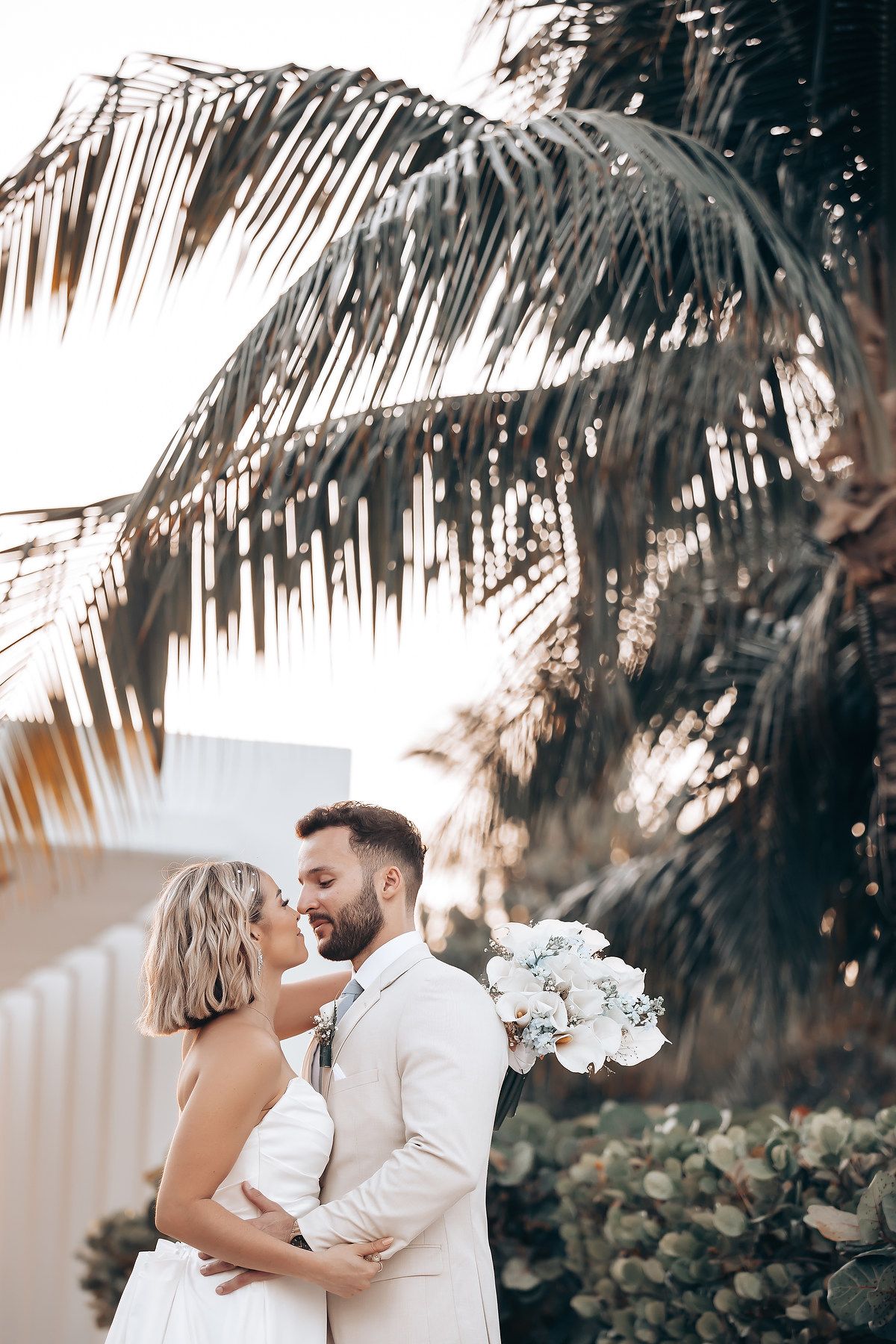 Romantic wedding photos among palm trees with elegant white floral decorations.