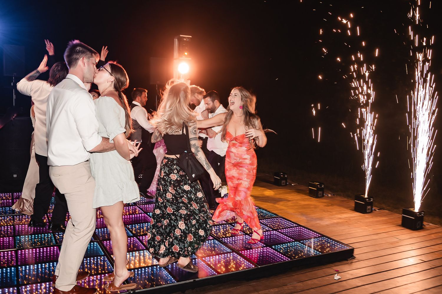 Wedding party dancing on an illuminated LED dance floor with sparkler effects.
