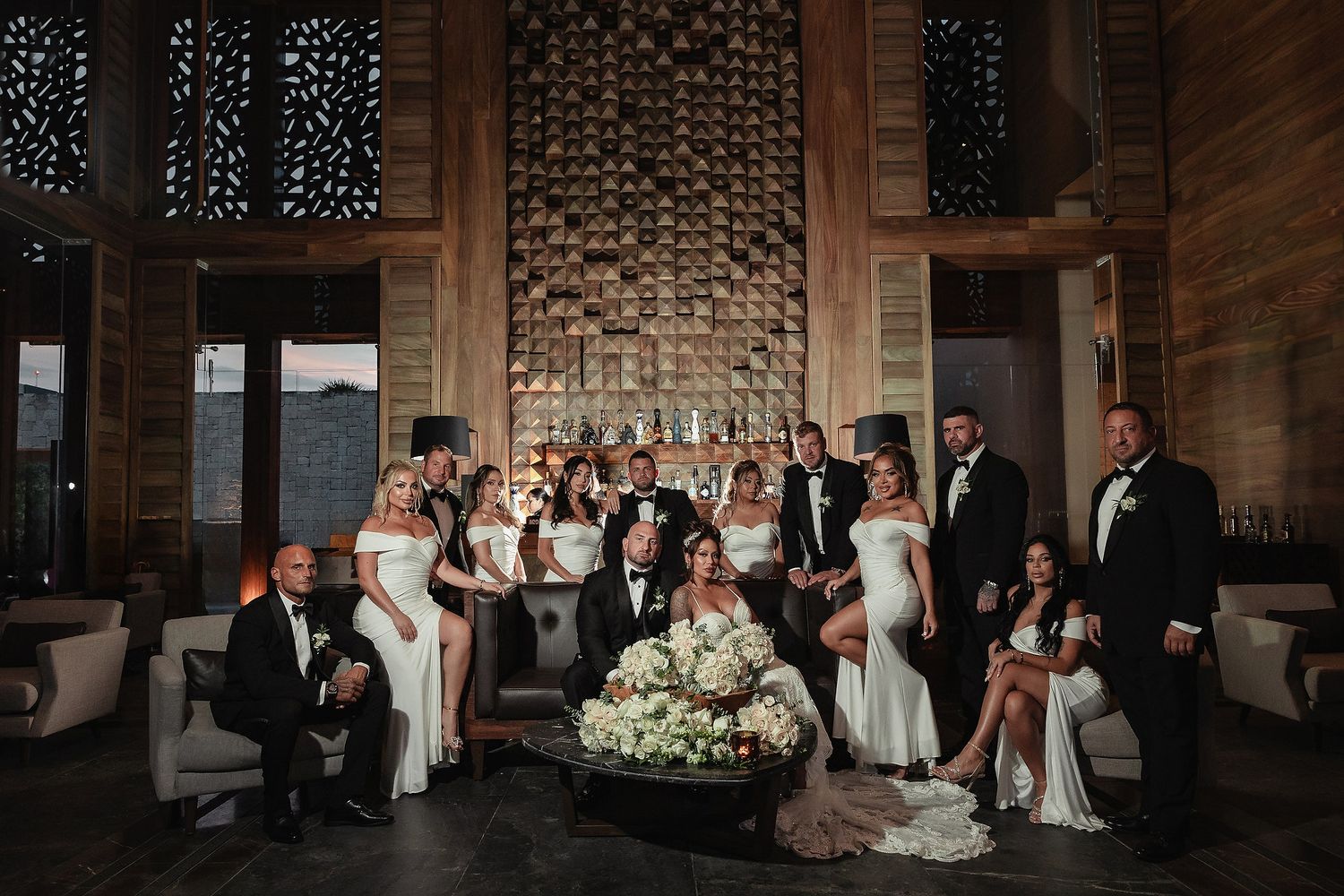Wedding party dances and celebrates during reception in elegant brick-walled venue with string lights overhead.