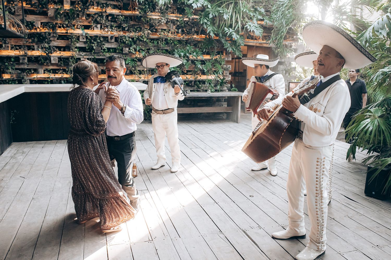 A couple shares a romantic first dance at a sunlit outdoor wedding venue surrounded by lush greenery and wooden decor.