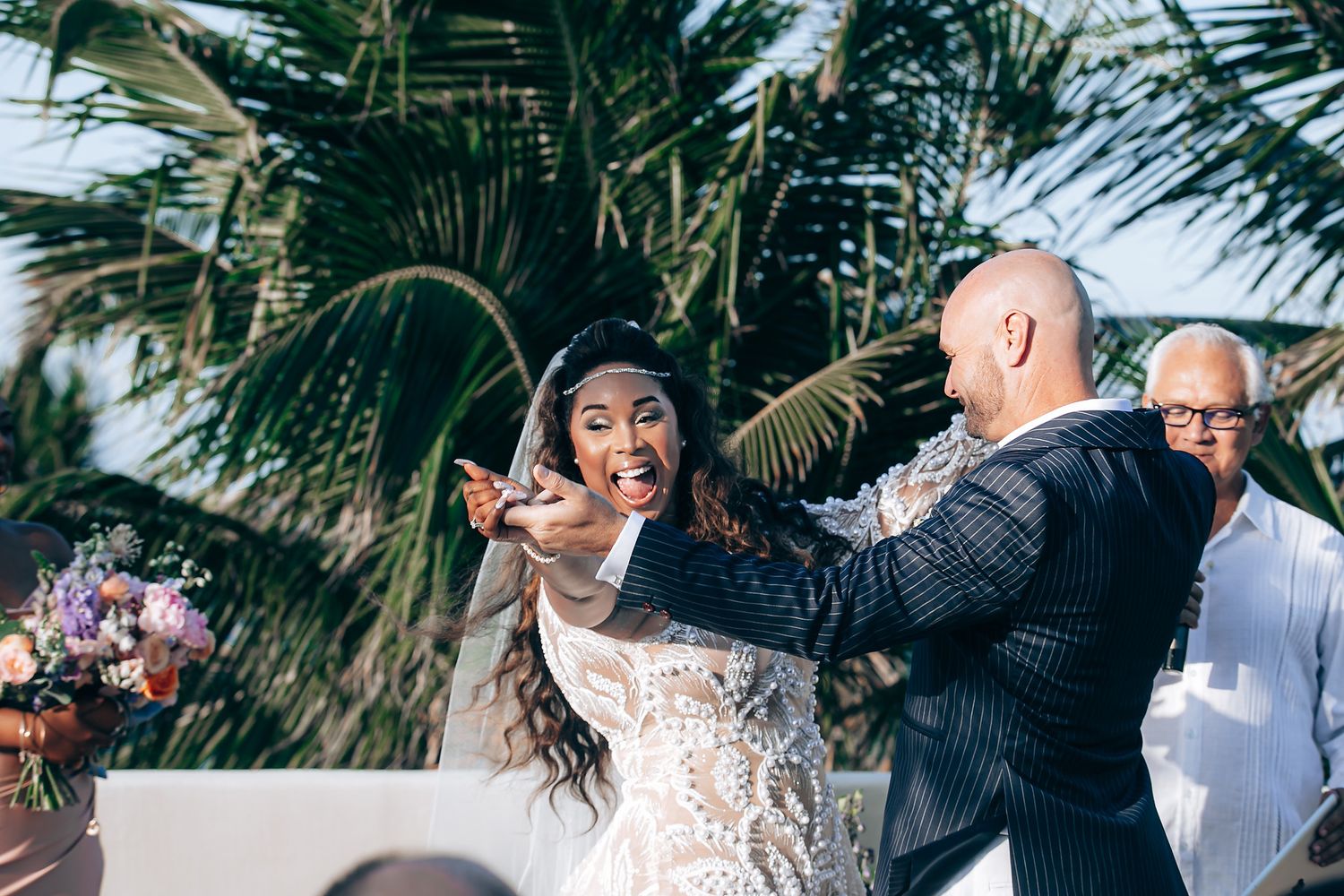 A couple dances together during an outdoor wedding celebration with palm trees in the background.