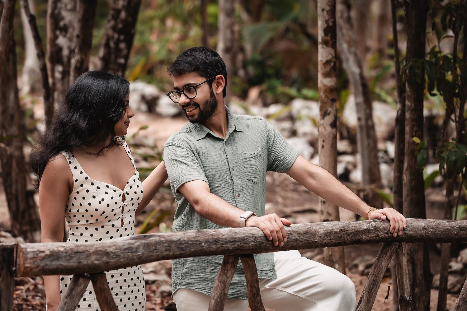 A couple in coordinated outfits shares joyful moments along a rustic wooden fence.