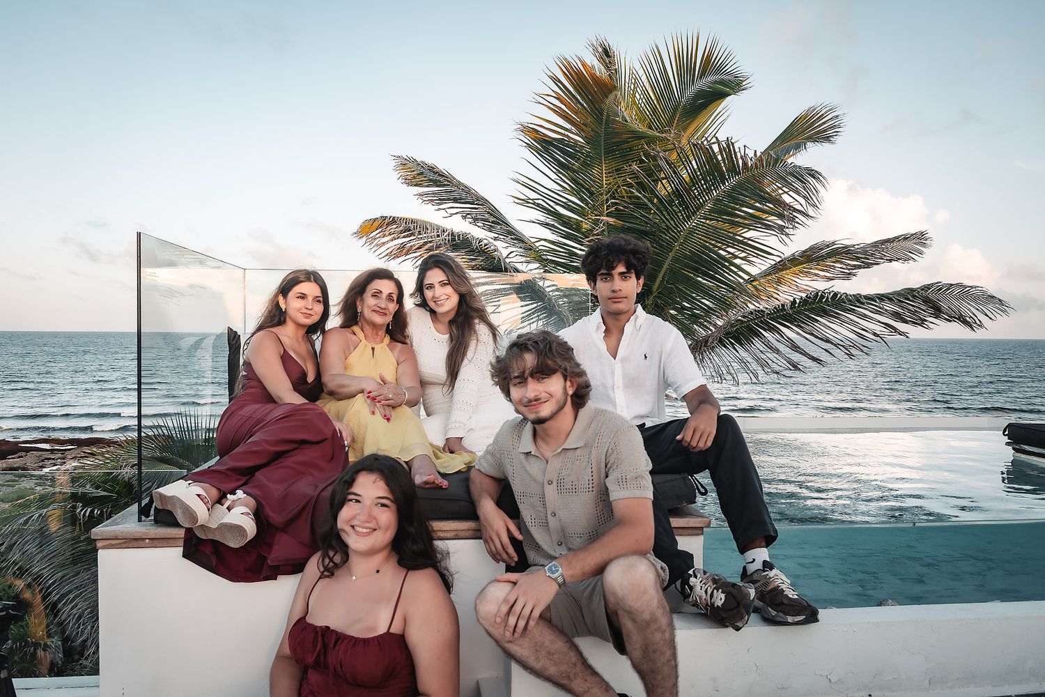 Casual group photo session on a beachfront wall with palm trees and ocean views.