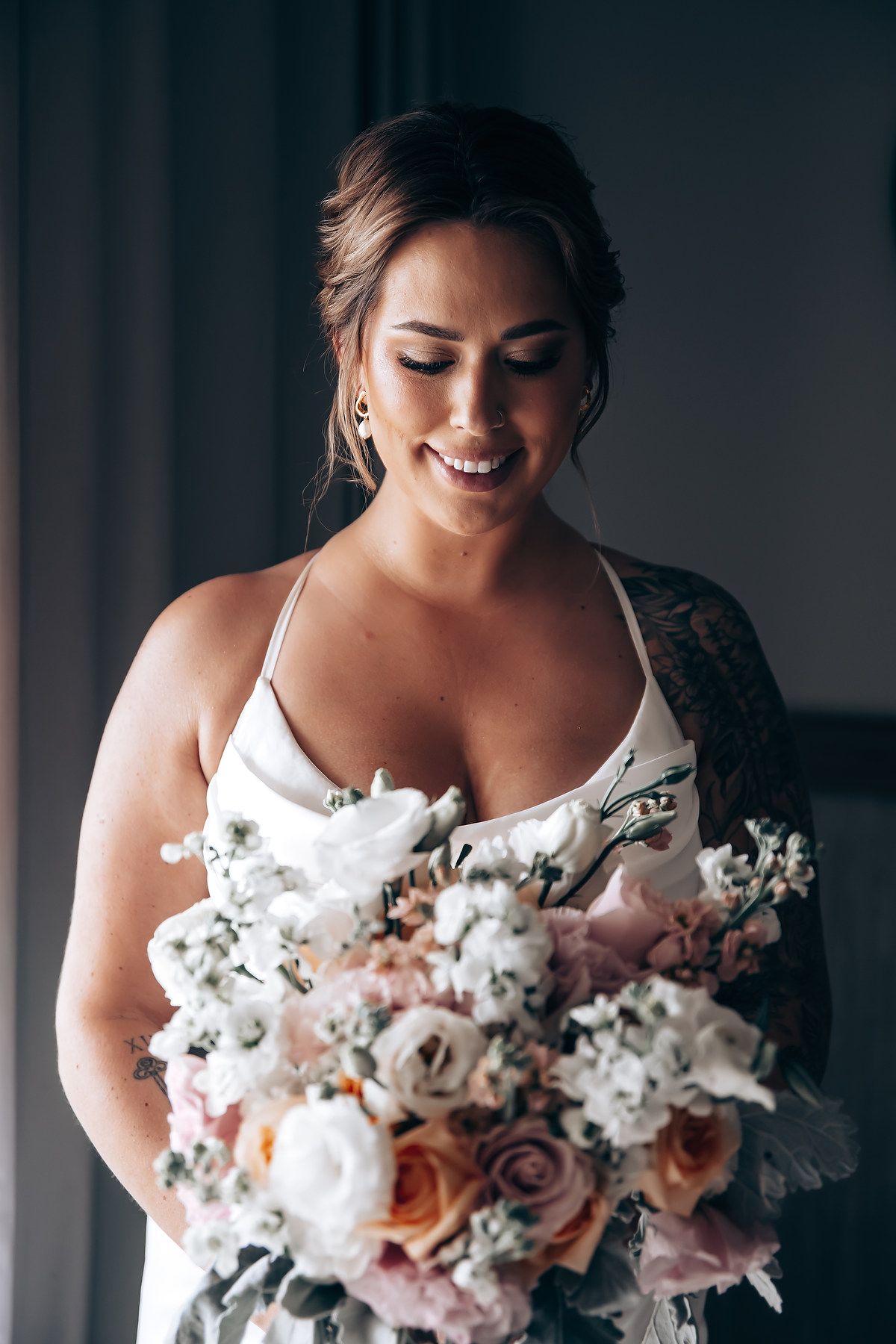 A bride in a white wedding dress smiles while holding a beautiful bouquet of white and pink flowers.