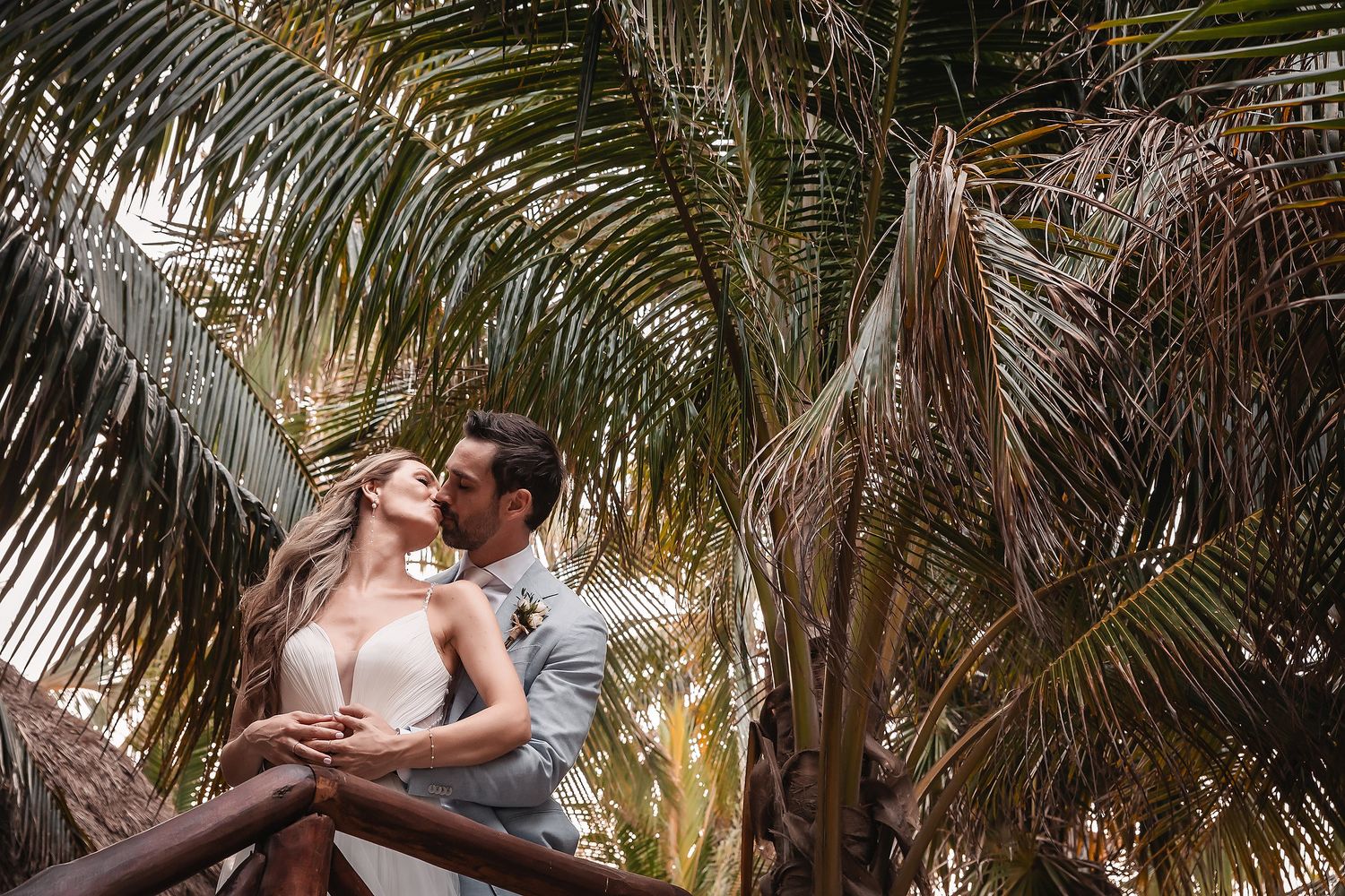 Gentle embrace between newlyweds surrounded by swaying palm fronds.