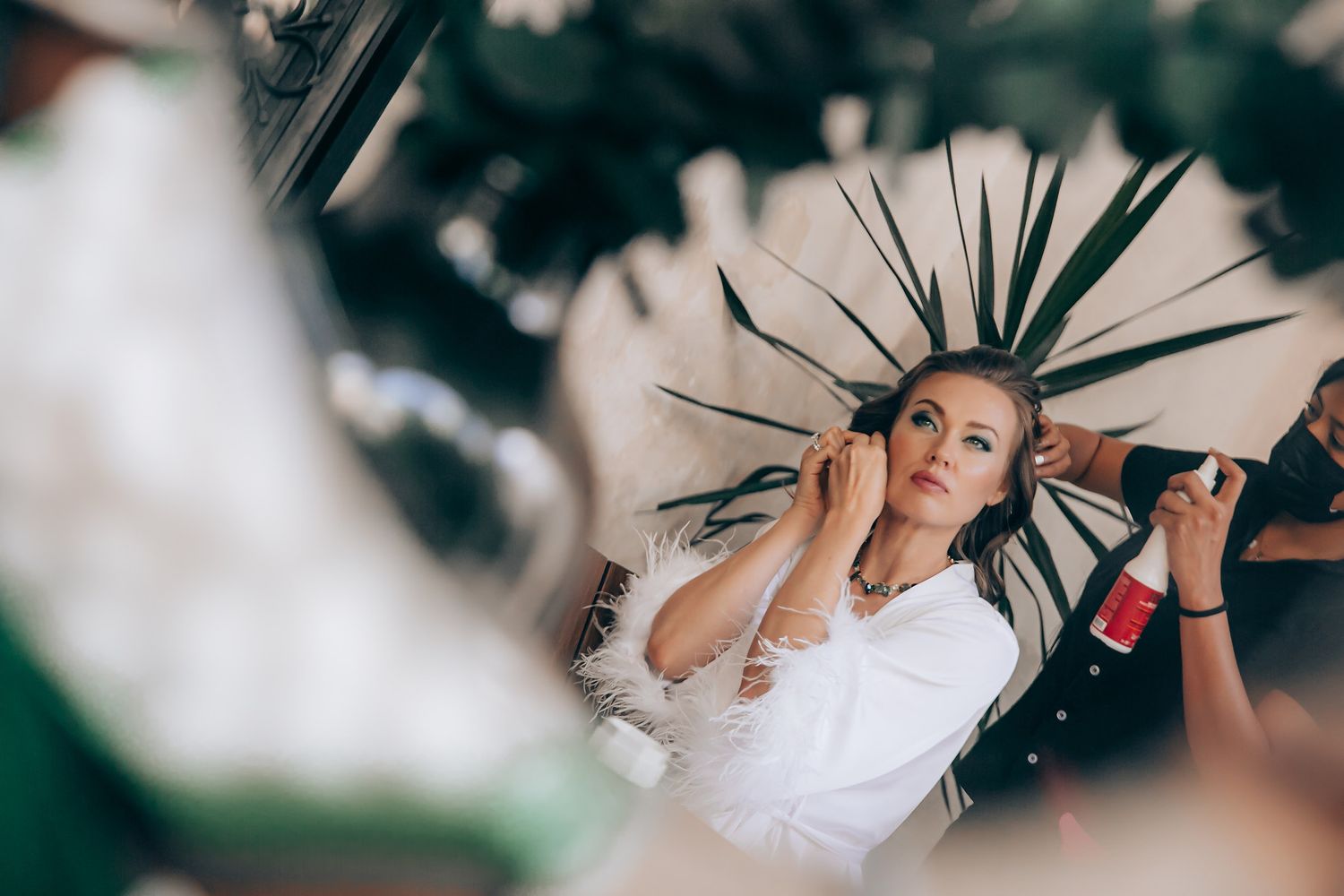 A person getting ready for a wedding with hair and makeup being styled against a blurred background.