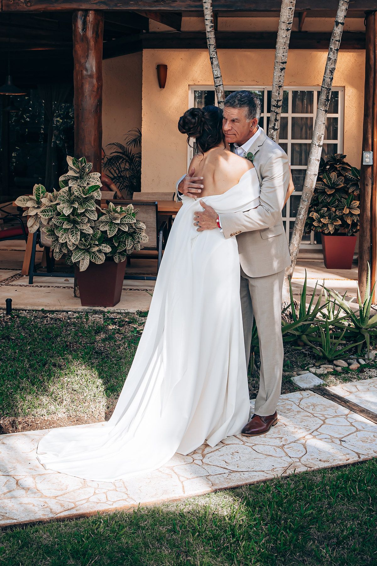 A couple embraces on their wedding day on a stone patio with potted plants and rustic decor in the background.