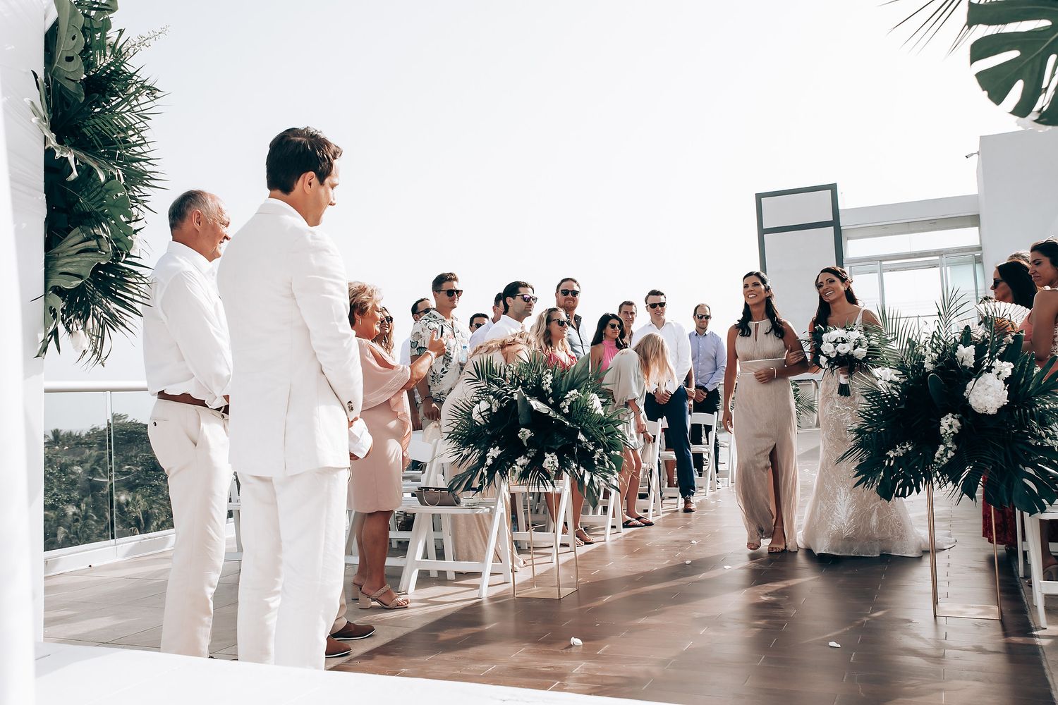 Wedding guests gathered at an oceanfront venue with white and tropical decor.