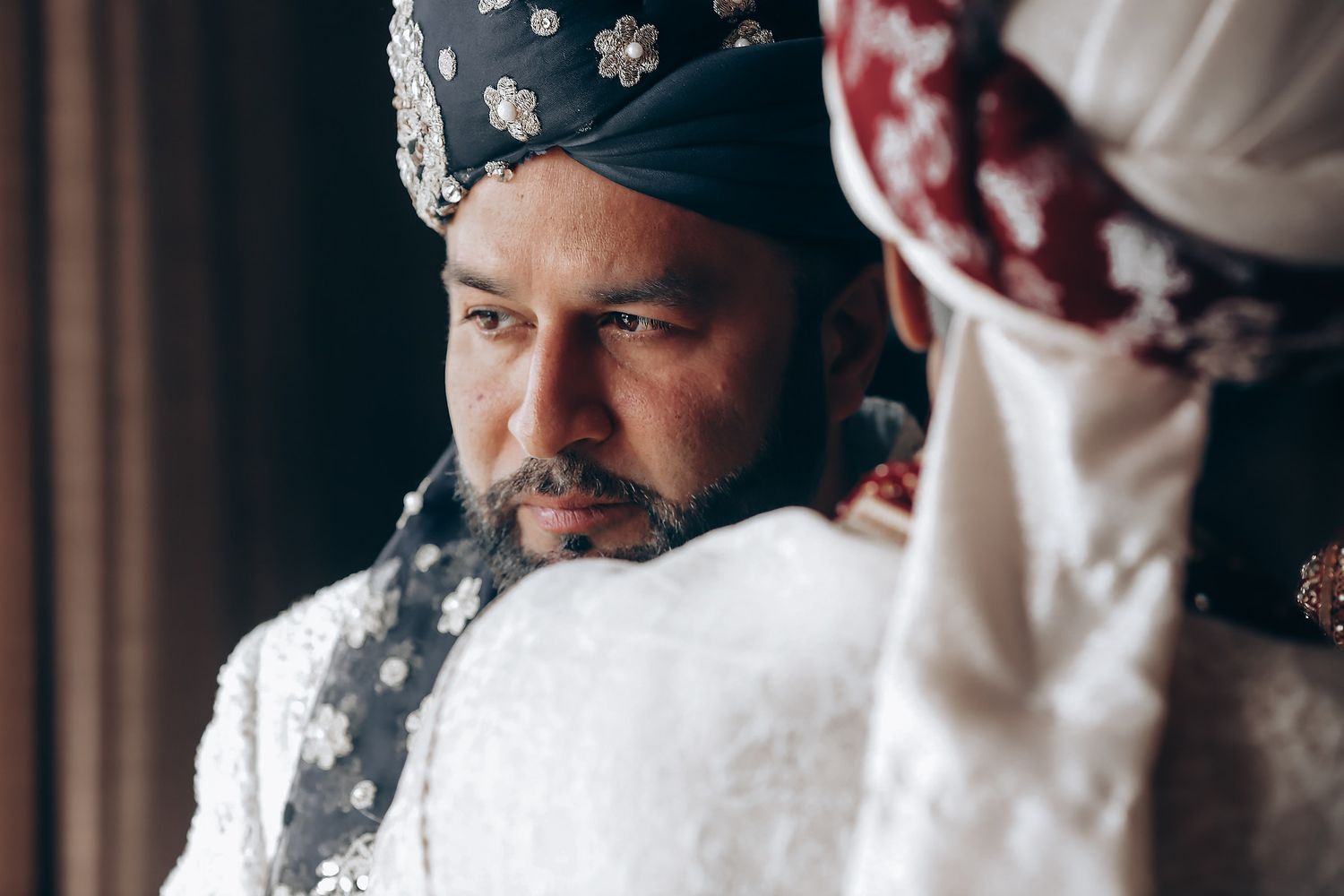 A person in traditional South Asian wedding attire with a decorated turban gazes thoughtfully to the side.