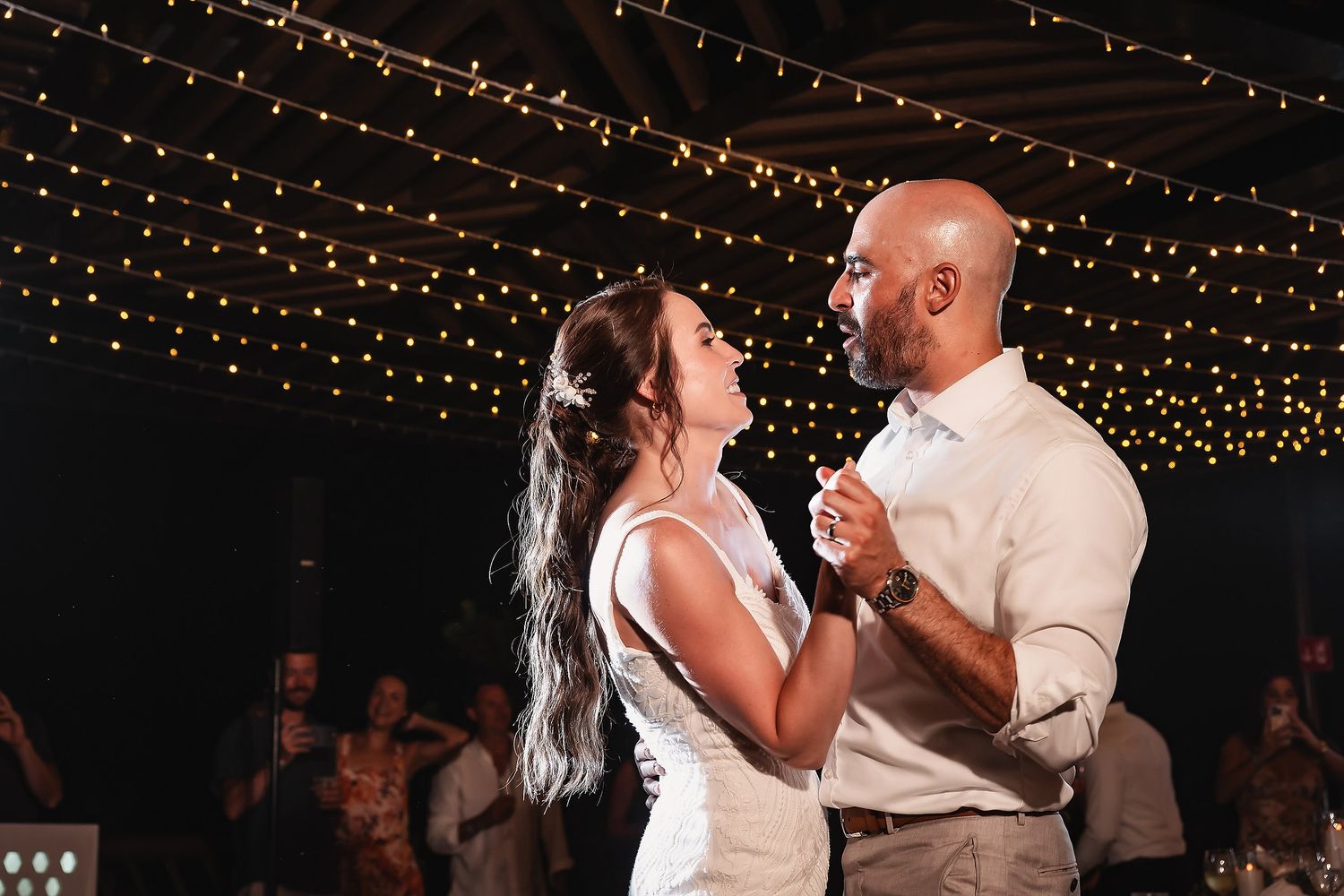 Couple shares a romantic dance under twinkling string lights at an evening wedding reception.