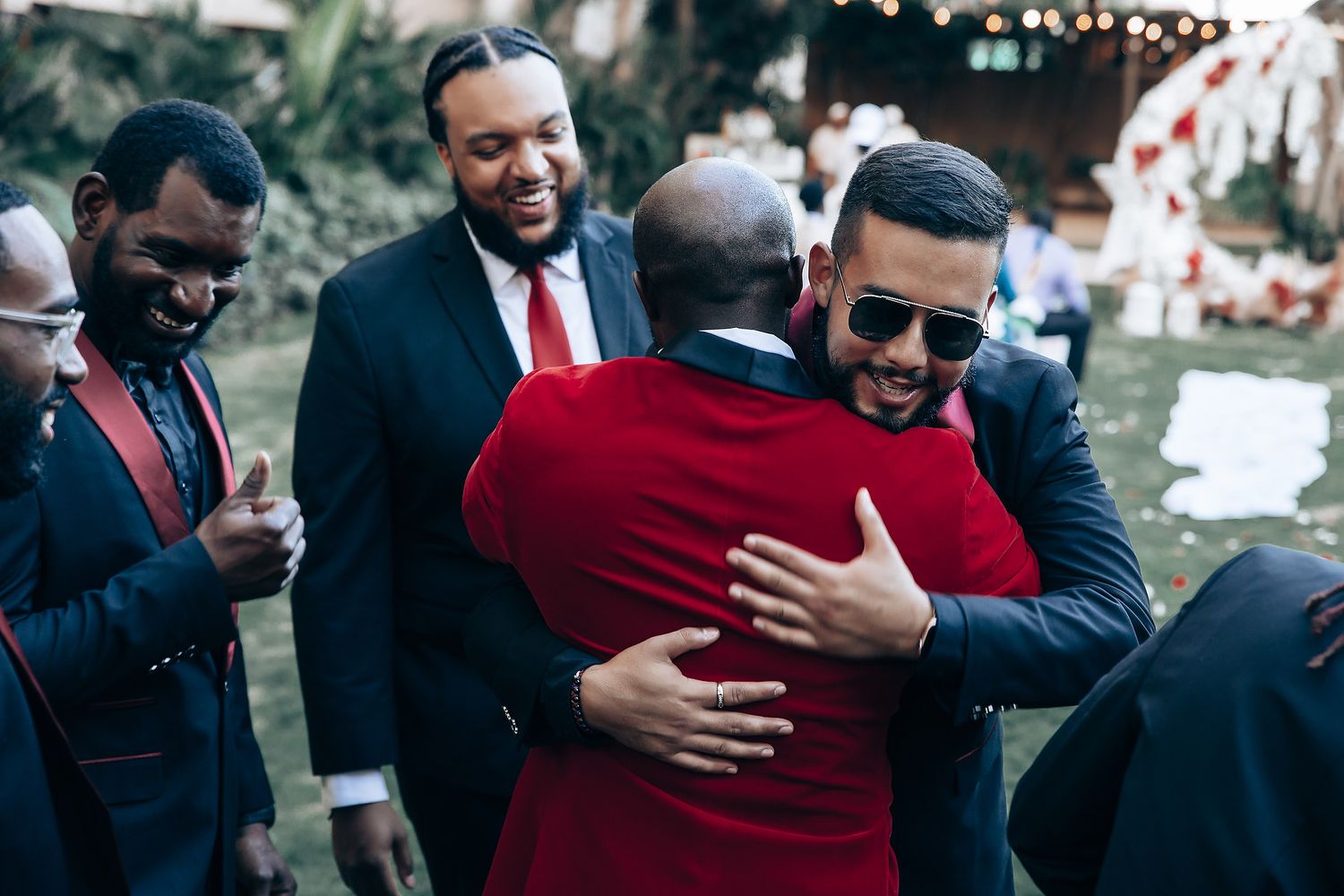Wedding guests in formal attire share warm hugs and smiles during an outdoor reception.