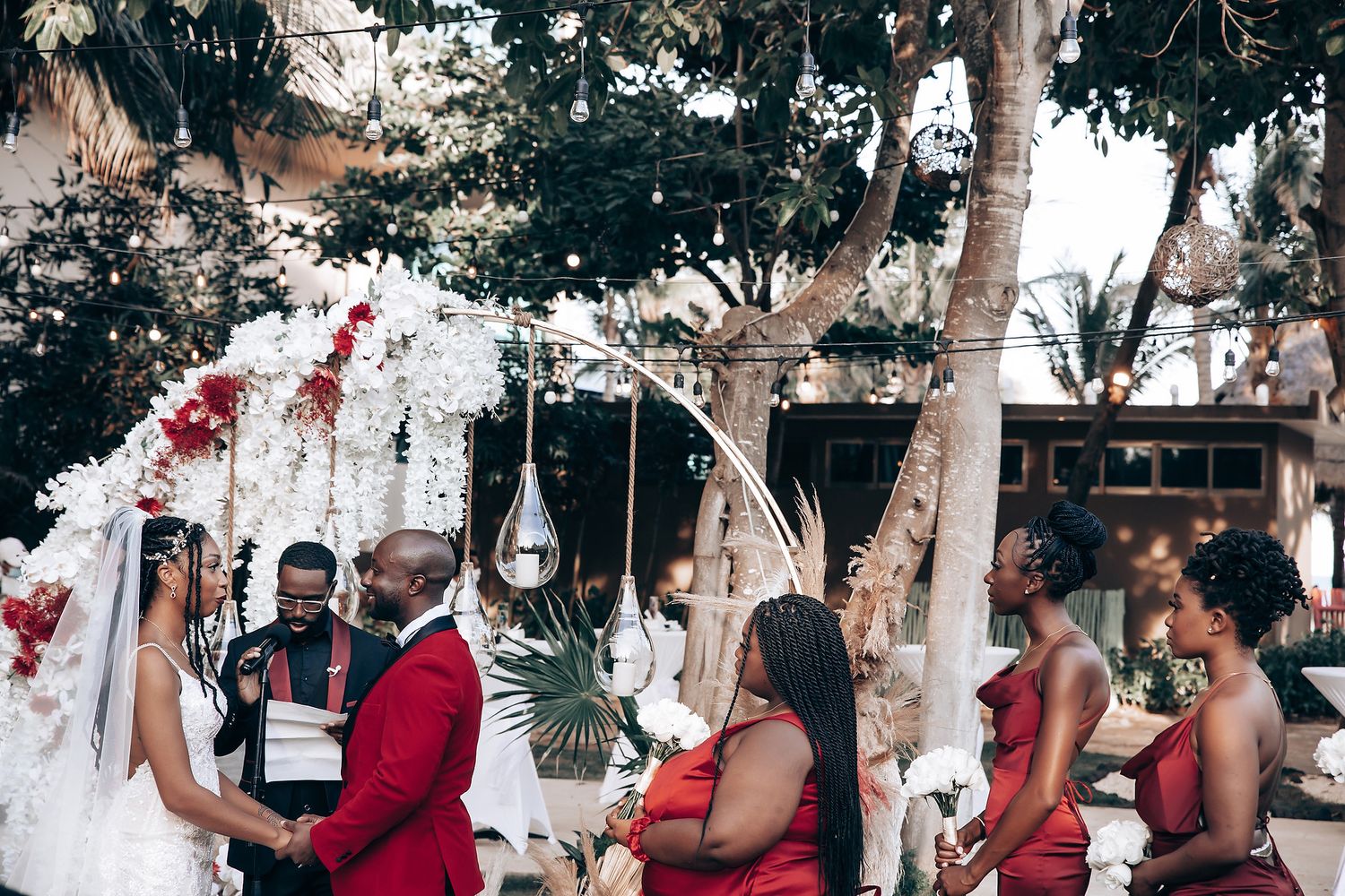 Wedding ceremony scene in an outdoor garden setting with red and white floral decor.