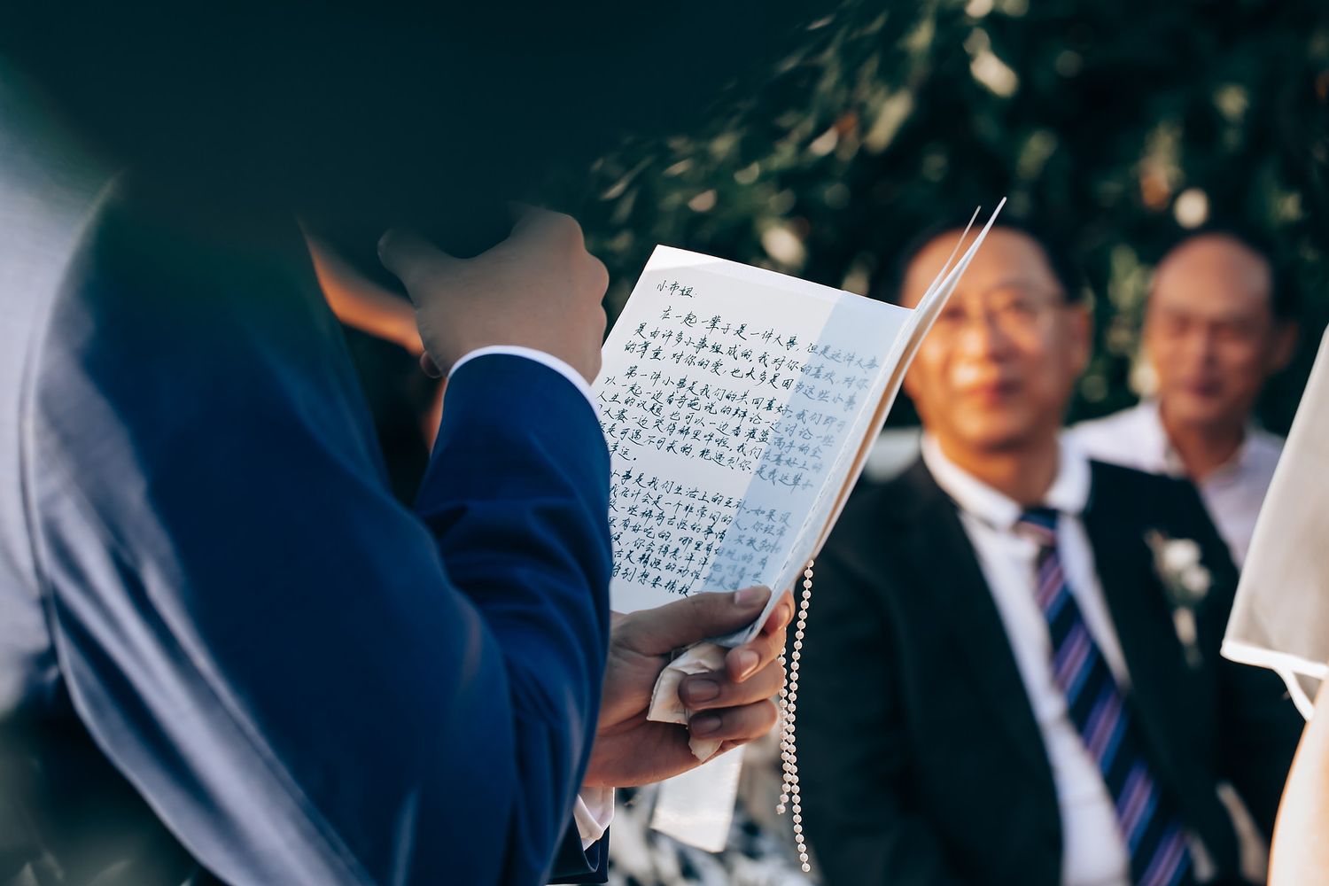 Wedding ceremony guests reading from paper programs outdoors.