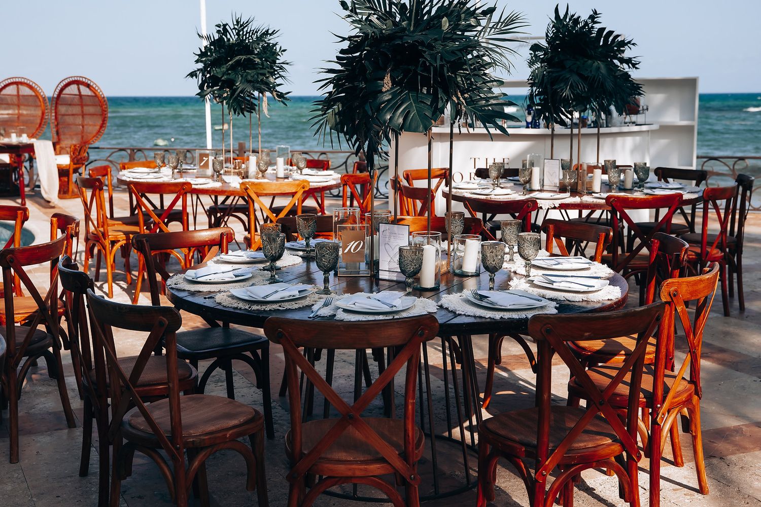 Beachfront wedding reception setup with rustic wooden tables and chairs overlooking the ocean.