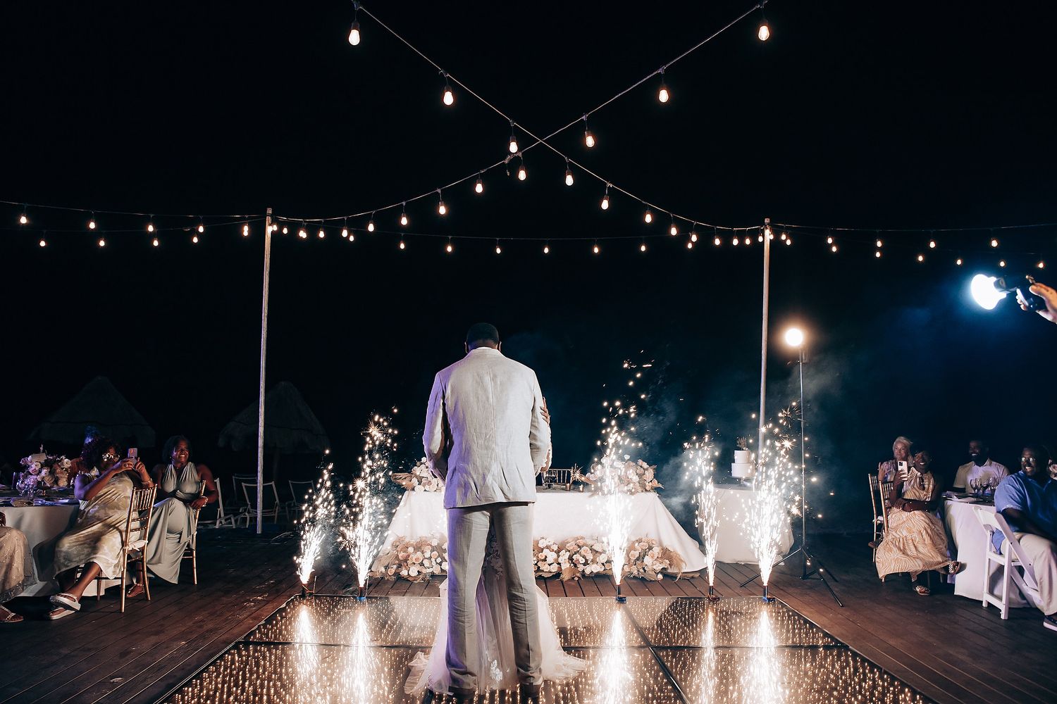 Nighttime wedding reception with sparklers and string lights creating magical atmosphere.