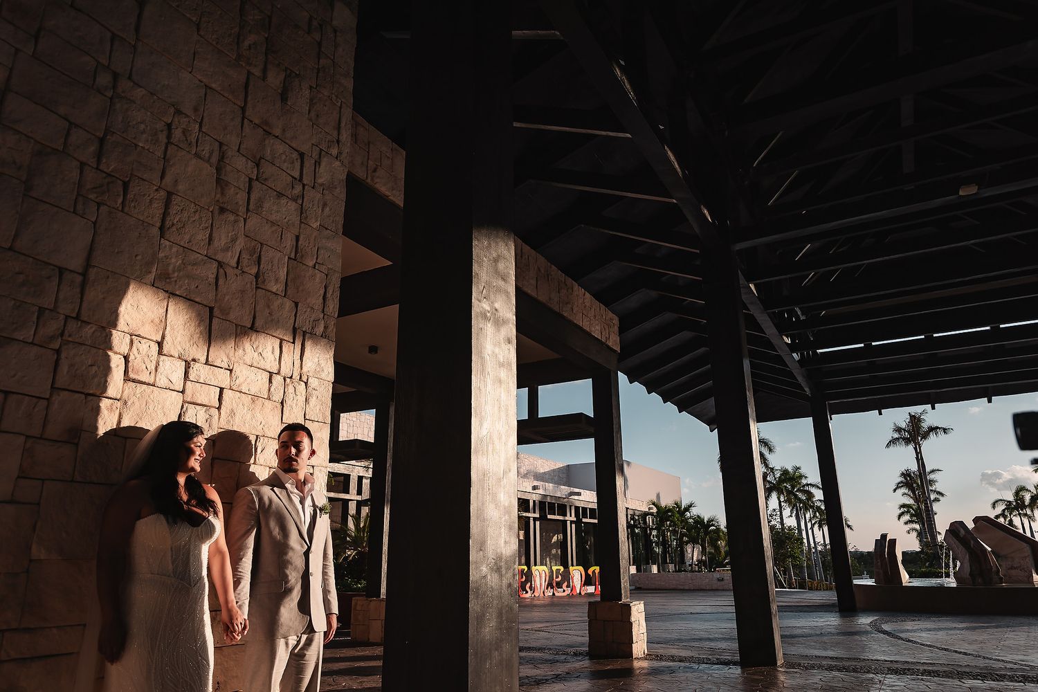Silhouettes of a couple standing under architectural columns with palm trees in the distance.
